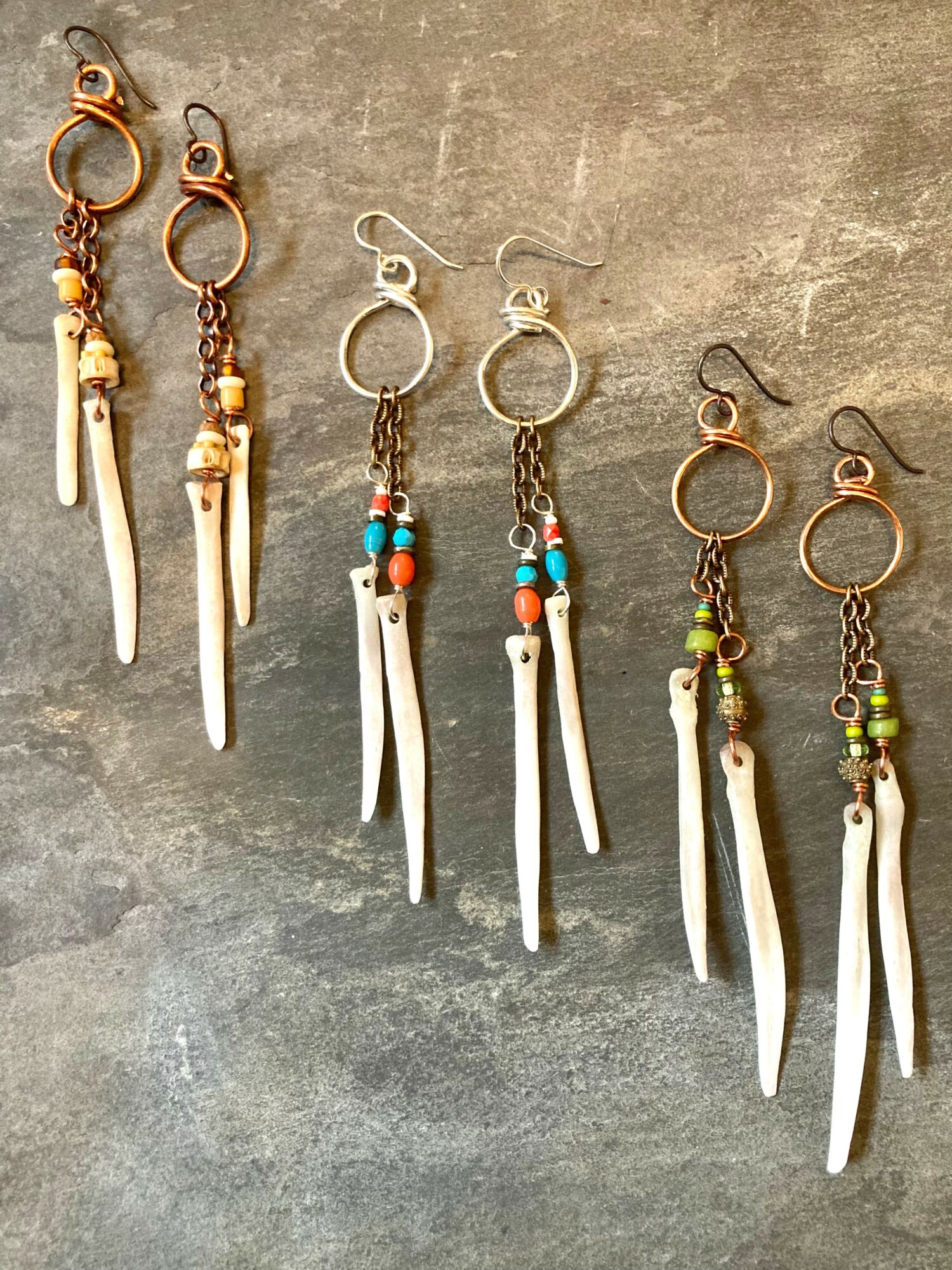 Four pairs of earrings with circular hooks, beads, and elongated white pendants, arranged on a gray surface.