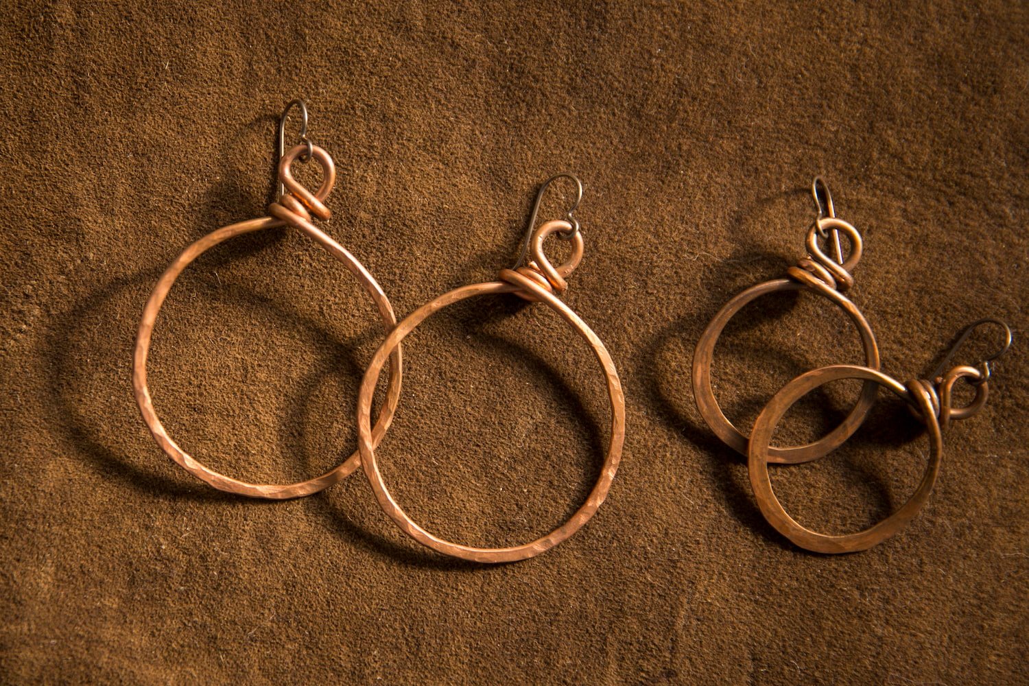 Two pairs of gold hoop earrings on a brown textured surface, with hooks attached to the hoops.