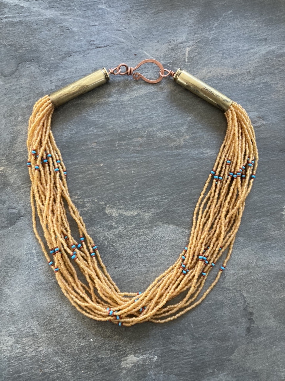 Beaded multi-strand necklace with gold-colored clasps and blue accents, laid on a gray surface.