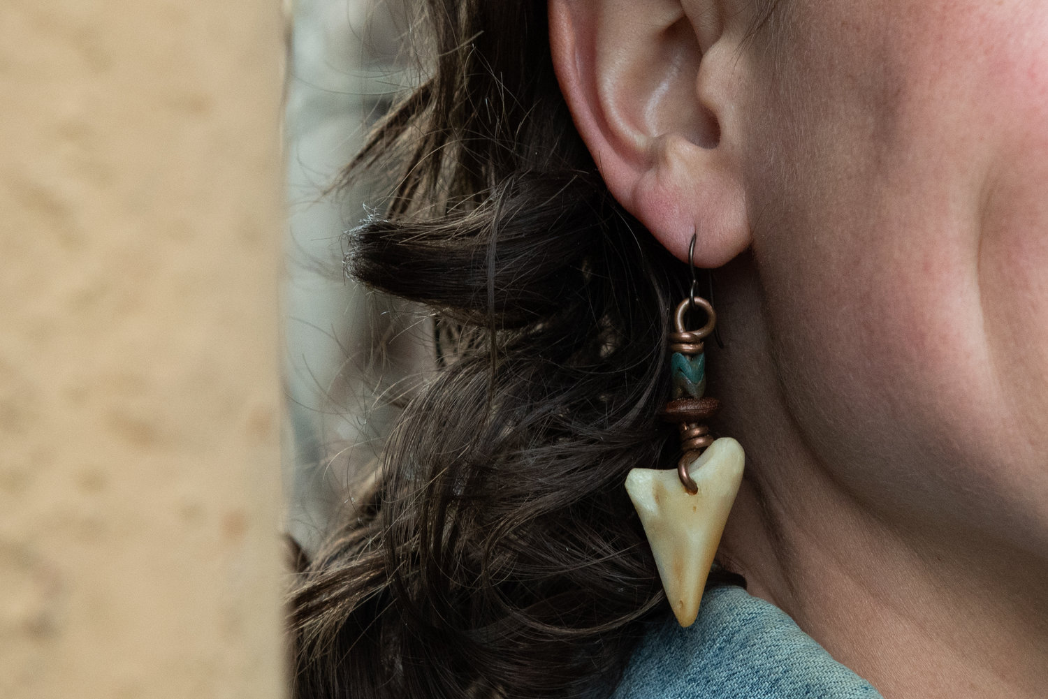 Close-up of a person's ear with a dangling earring, showing part of their face and hair.