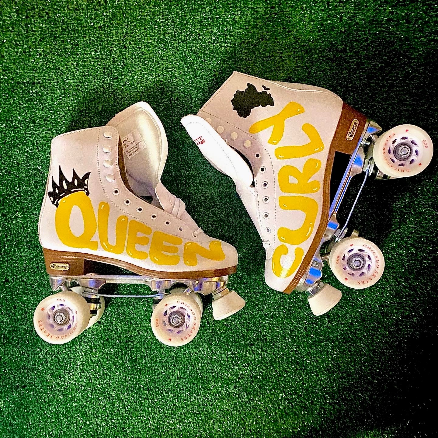 Pair of white roller skates with yellow and black lettering, placed on green surface, one skate upside down.