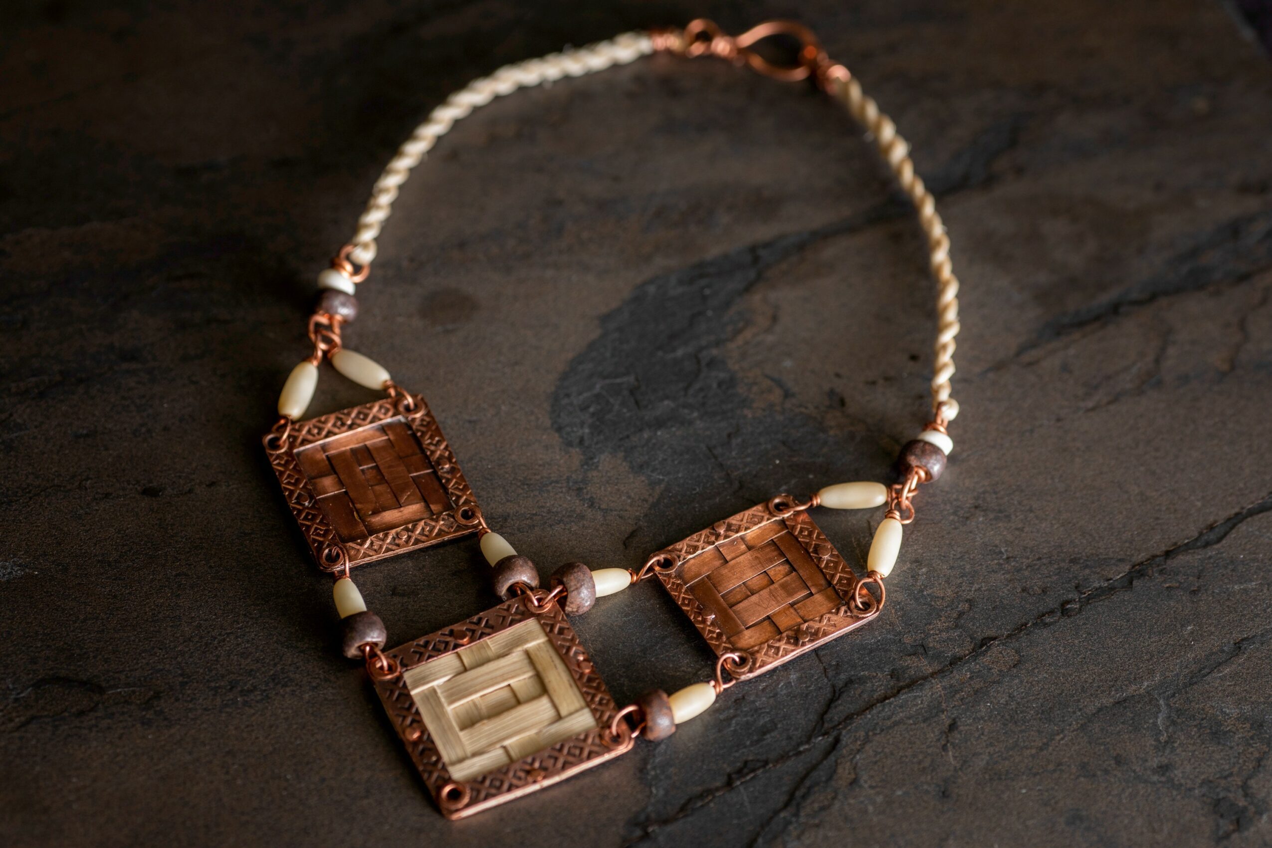 Necklace with rectangular pendants, beads, and a chain, placed on a dark wooden surface.