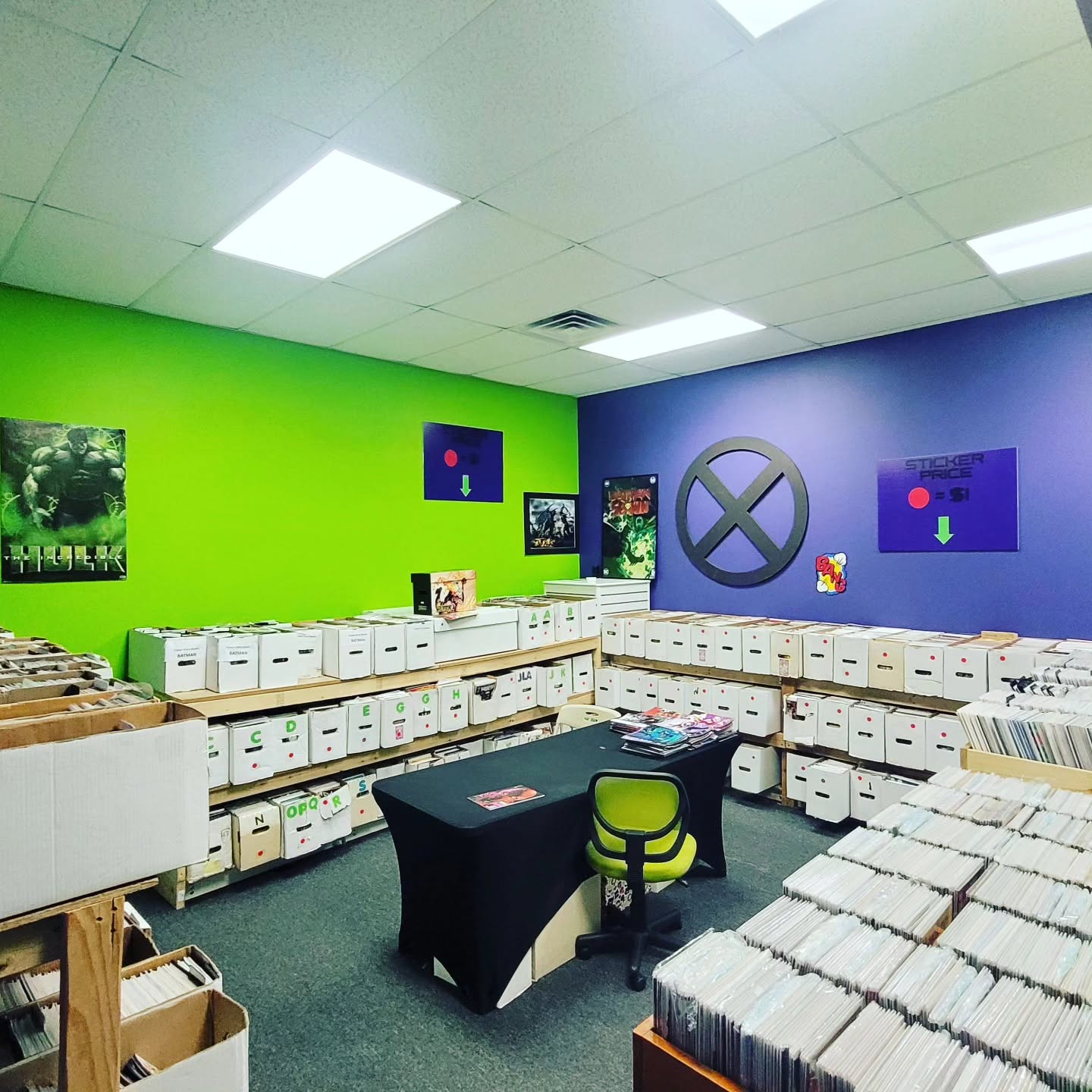 Room with green and purple walls, white storage boxes, a desk with a green chair, and artwork on the walls.