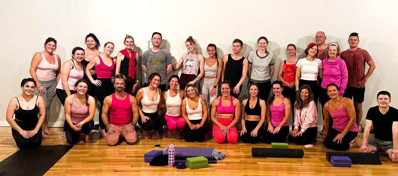 Group of women and men in workout clothes posing in a fitness studio with exercise mats and equipment.