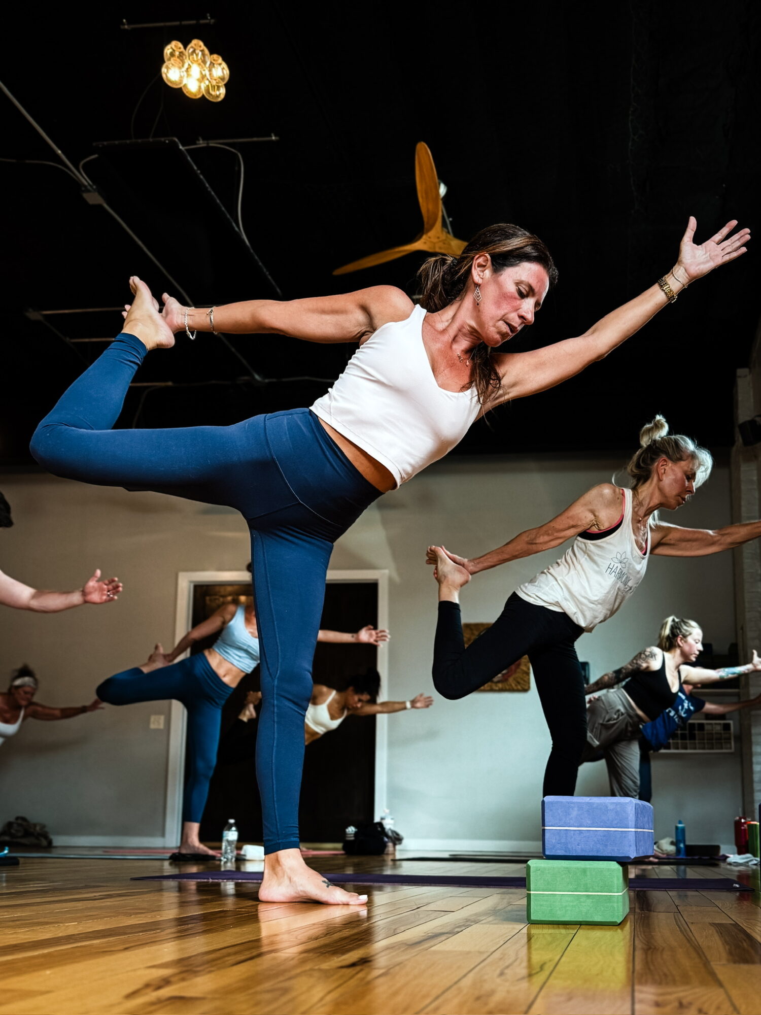 Woman balancing on one leg with arms extended, participating in a yoga class with children in the background.