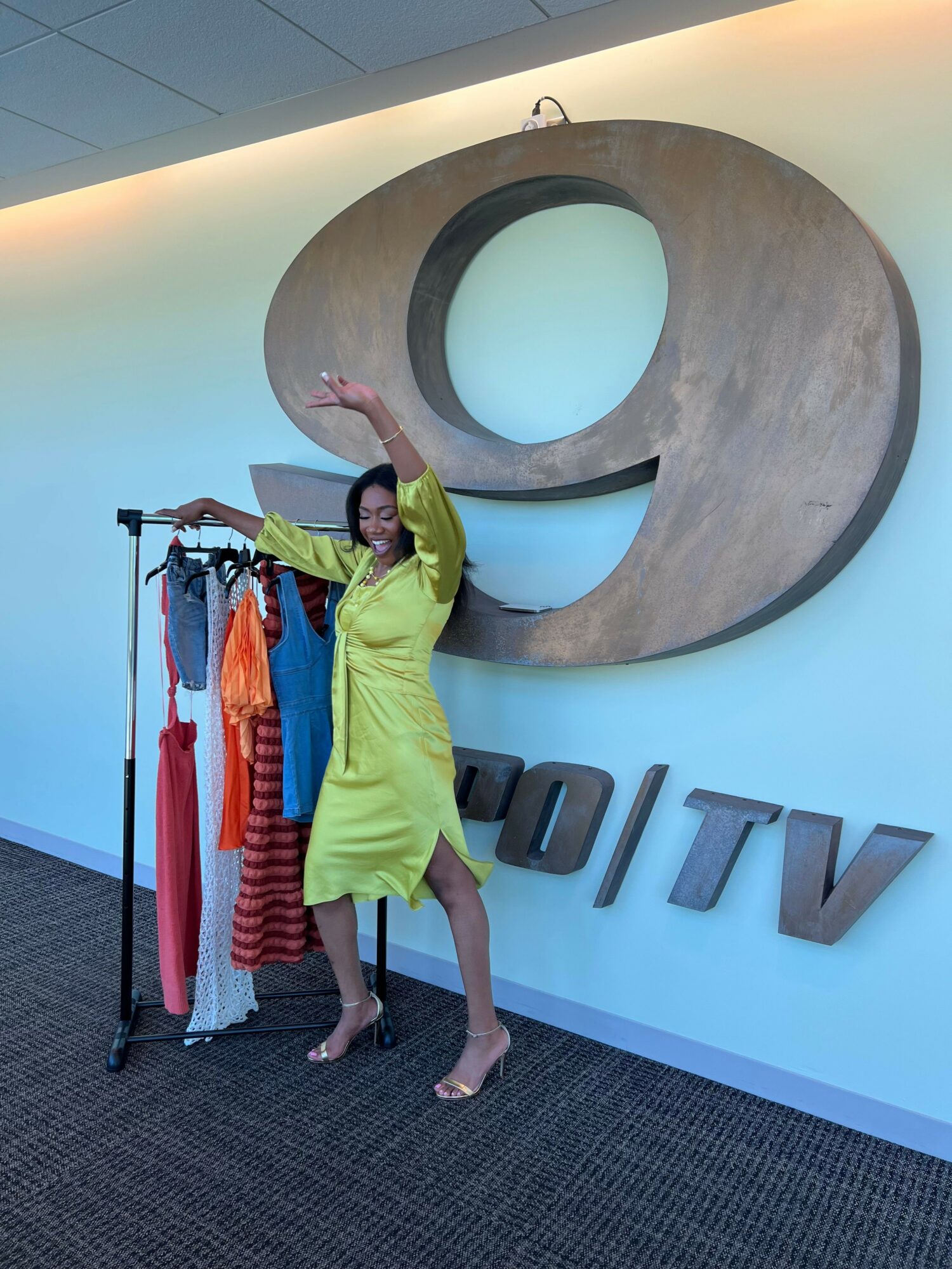 Person in yellow dress standing next to clothing rack in store, with large logo on wall behind them.