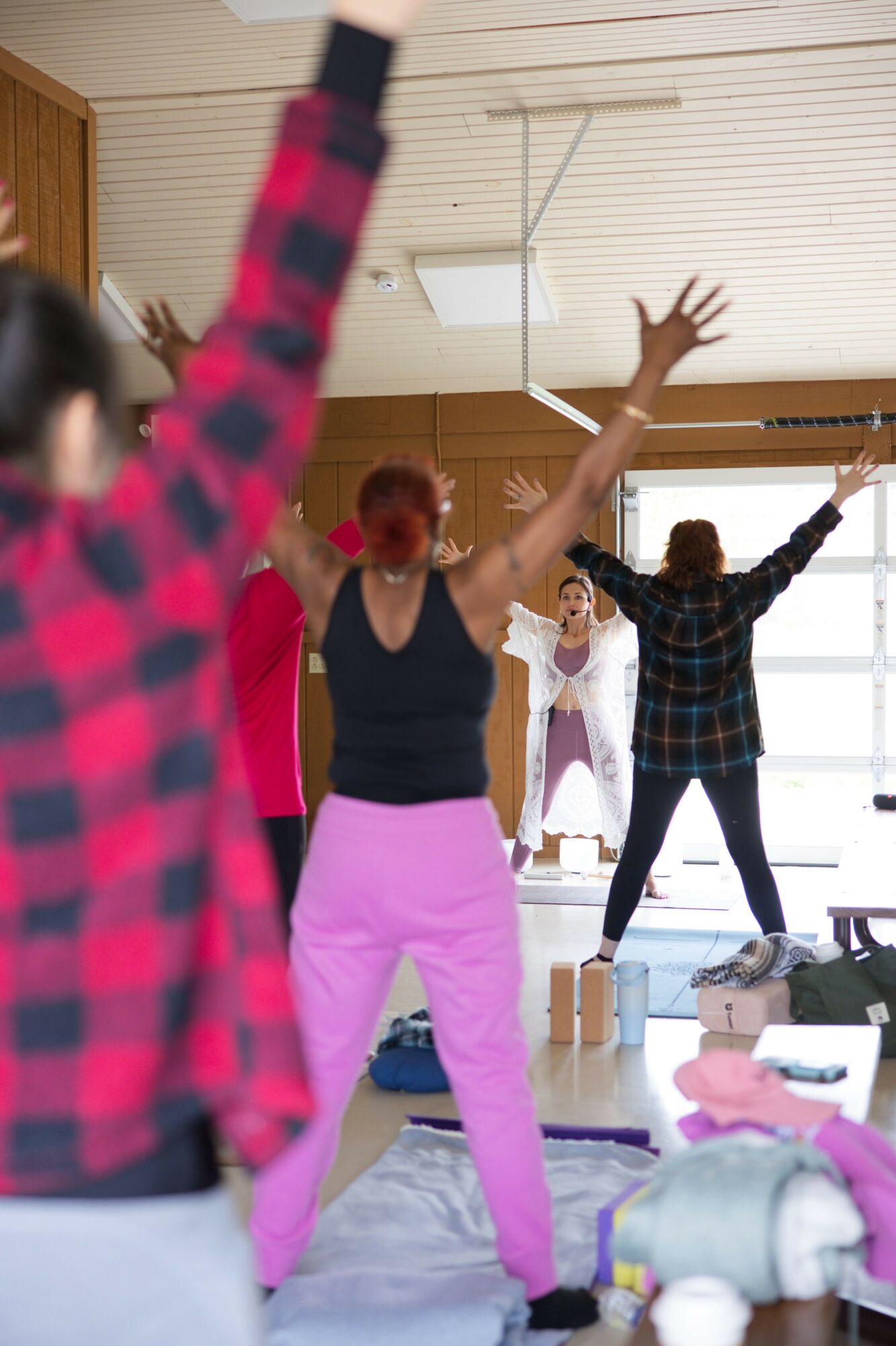 Group of people dancing indoors, some with arms raised, in a room with wooden walls and ceiling.