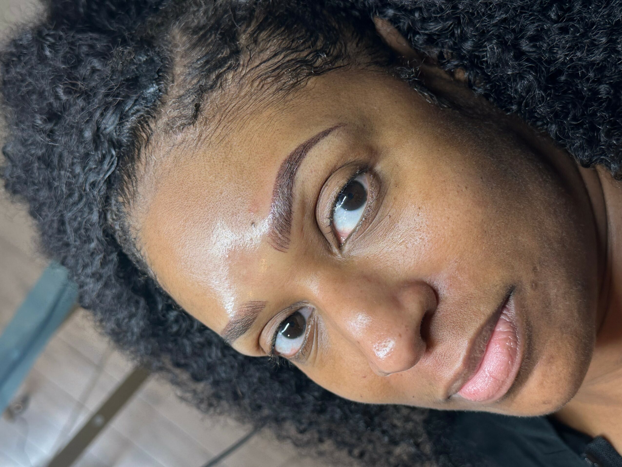 Close-up of a woman's face with curly hair, looking sideways, with natural lighting and a neutral background.