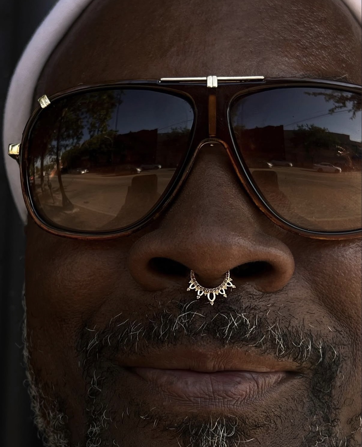Close-up of a person's face with sunglasses and a nose ring, showing only the nose and mouth area.