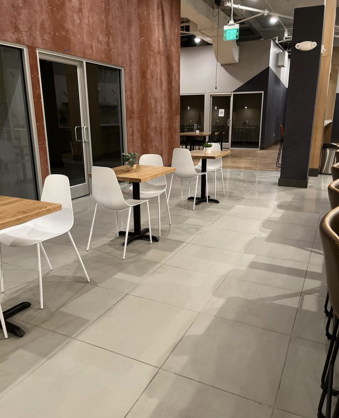Empty indoor space with tables and chairs, large windows, and a polished tiled floor.