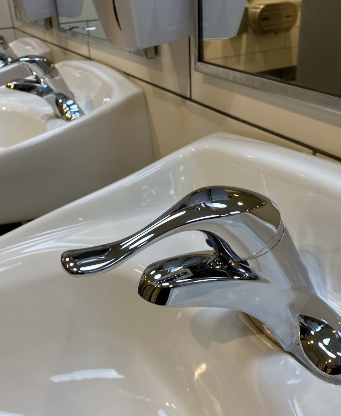 Close-up of a shiny chrome faucet on a white sink with a mirror in the background.