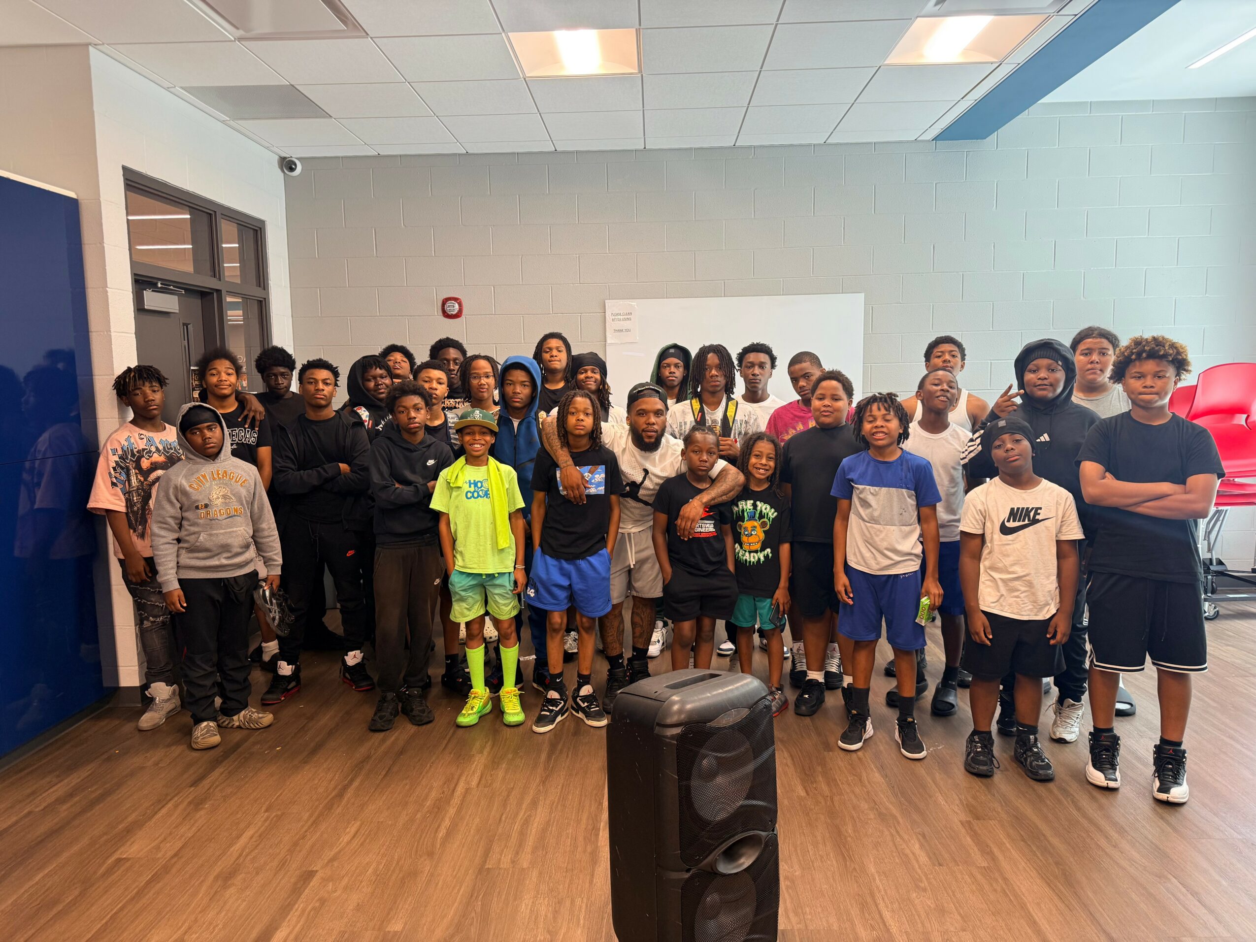 Group of children and adults standing in a room with a whiteboard, some smiling and looking at the camera.