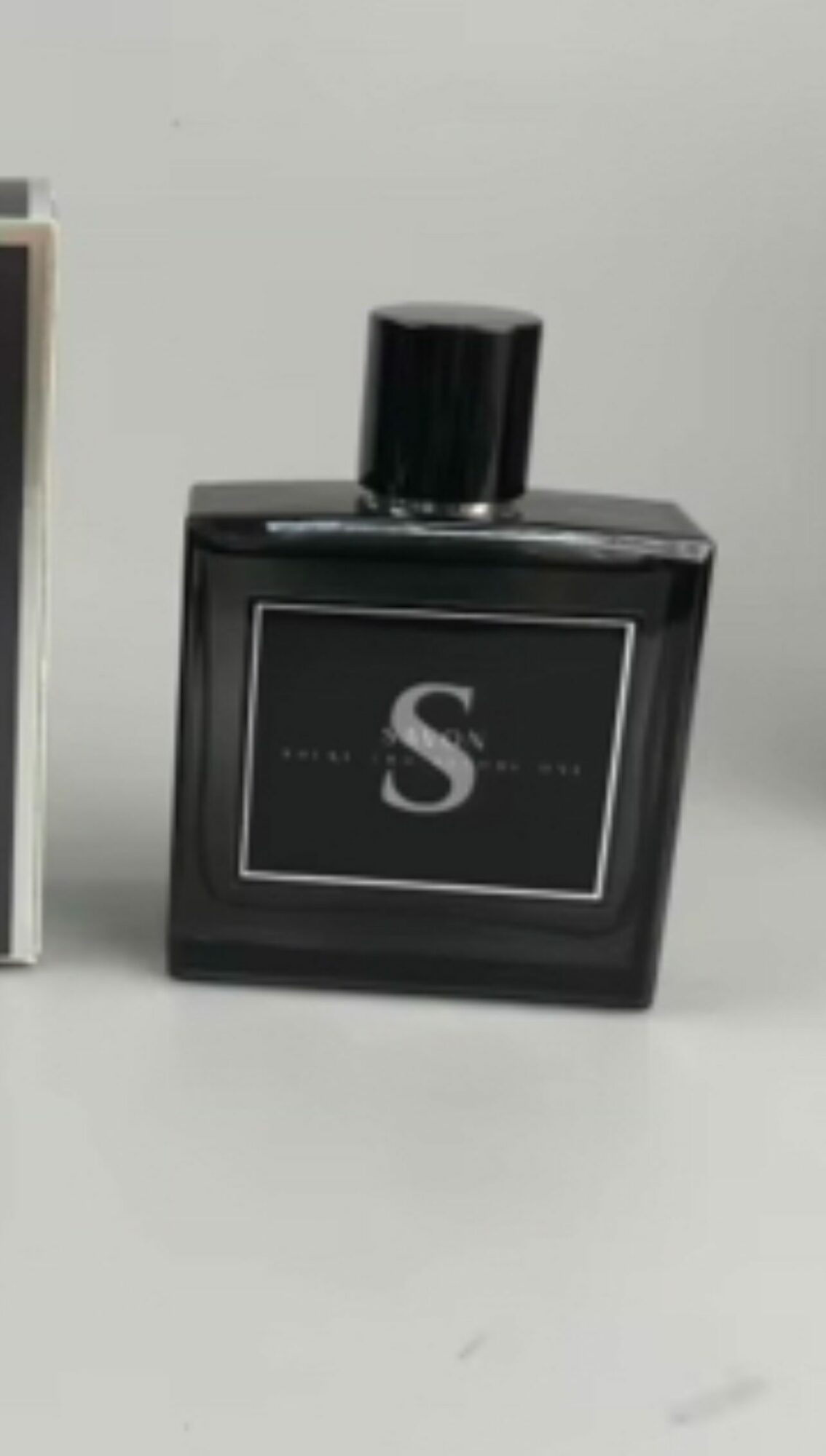 Black perfume bottle with a large letter 'S' on the label, placed on a white surface.