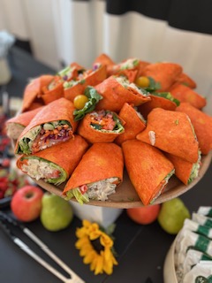 Plate of sliced wraps filled with vegetables and meat, garnished with yellow cherry tomatoes and greens, on a black table.