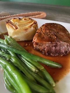 Cooked beef, green beans, and a baked potato with toppings on a plate.