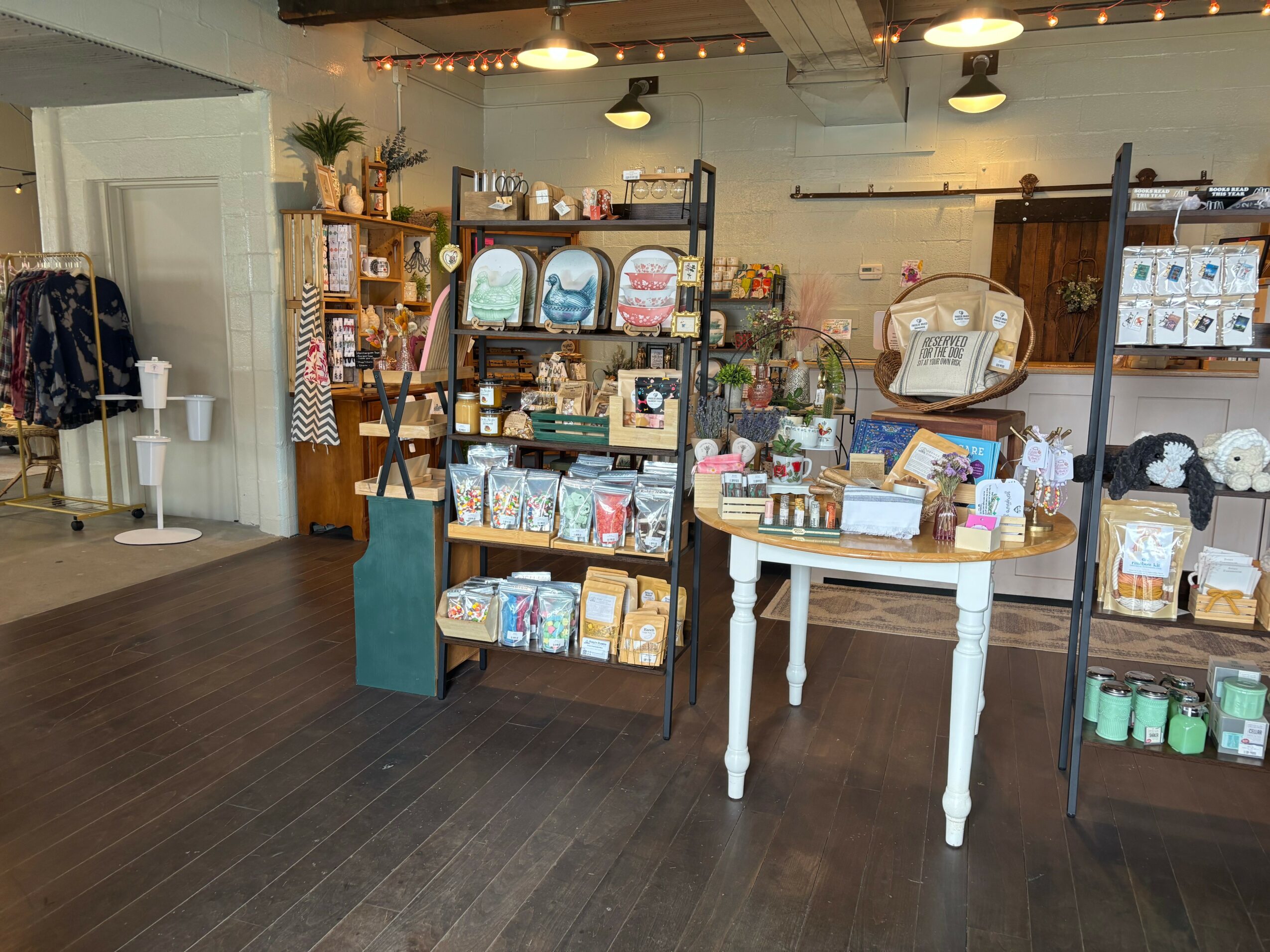 Interior of a store with shelves displaying various products, a white table, and a wooden floor.