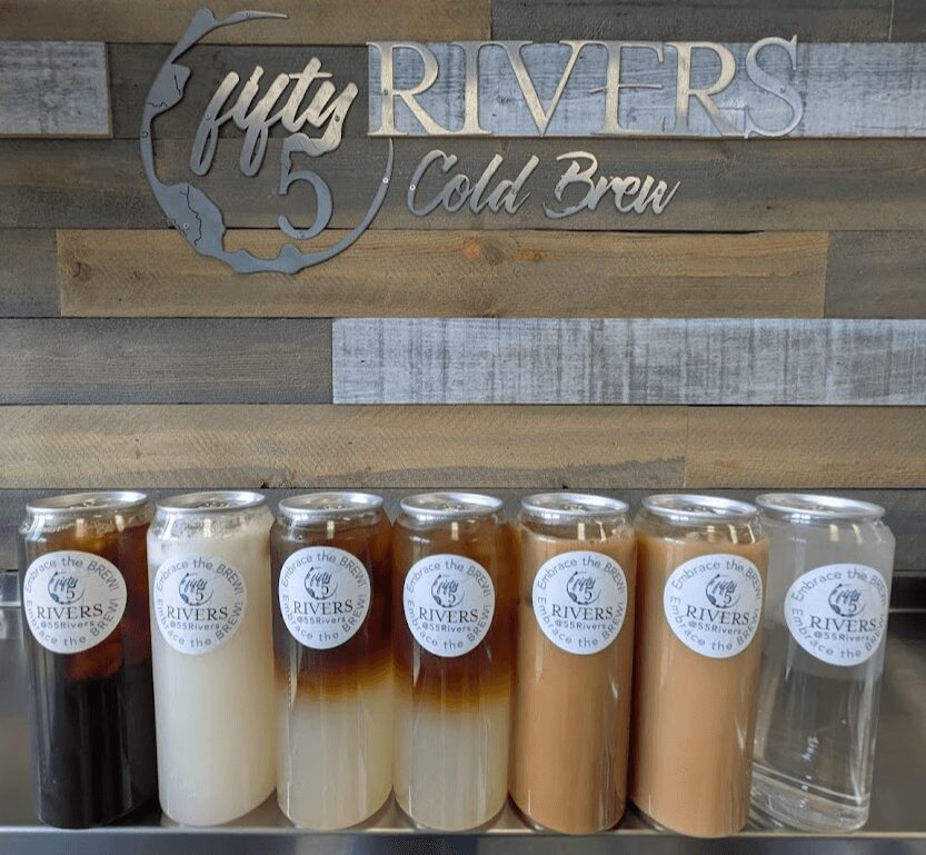 Seven cans of cold brew coffee with different colors and labels, displayed in a row on a wooden surface.