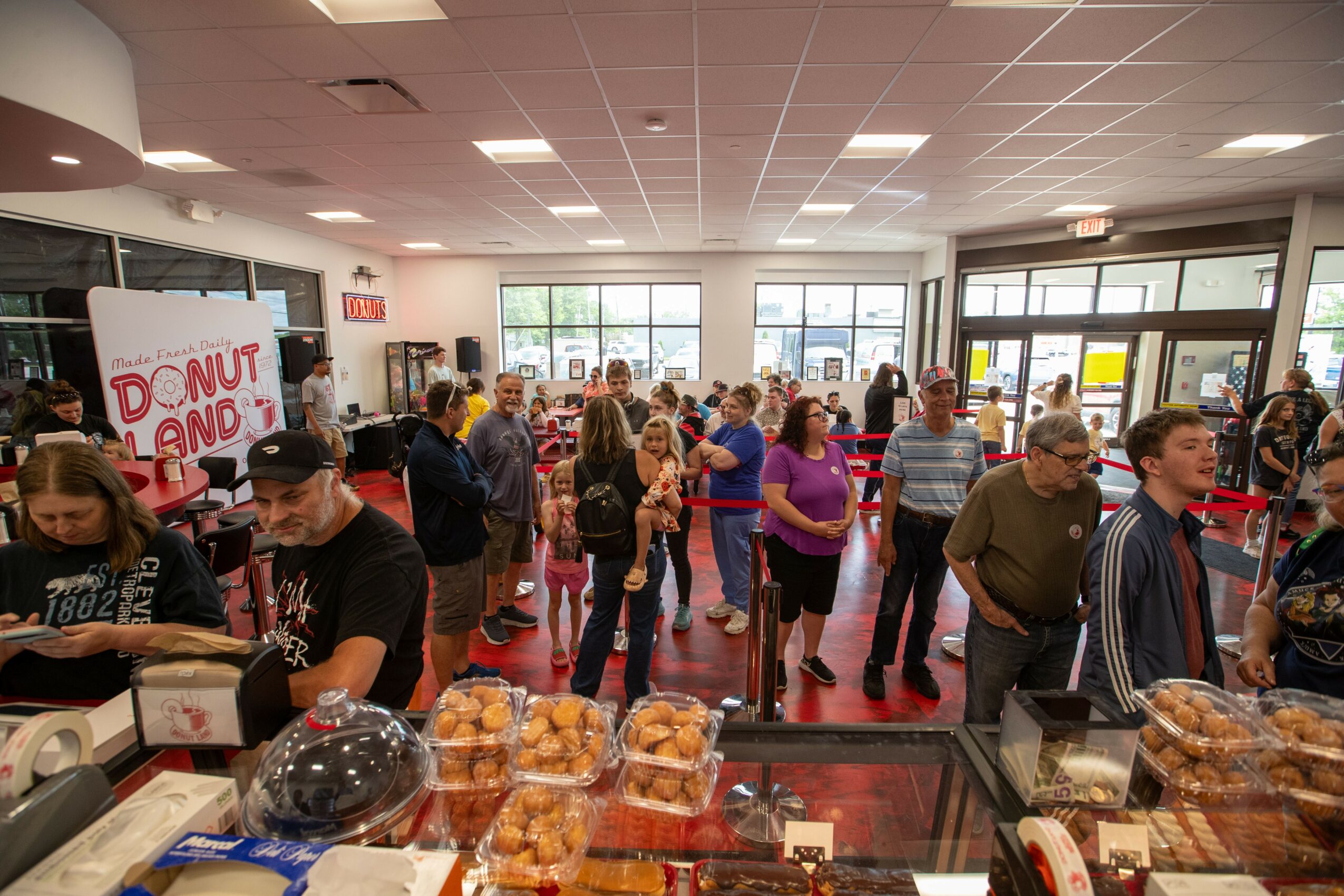 Crowded bakery with people shopping and baked goods on display, inside a well-lit store with large windows.