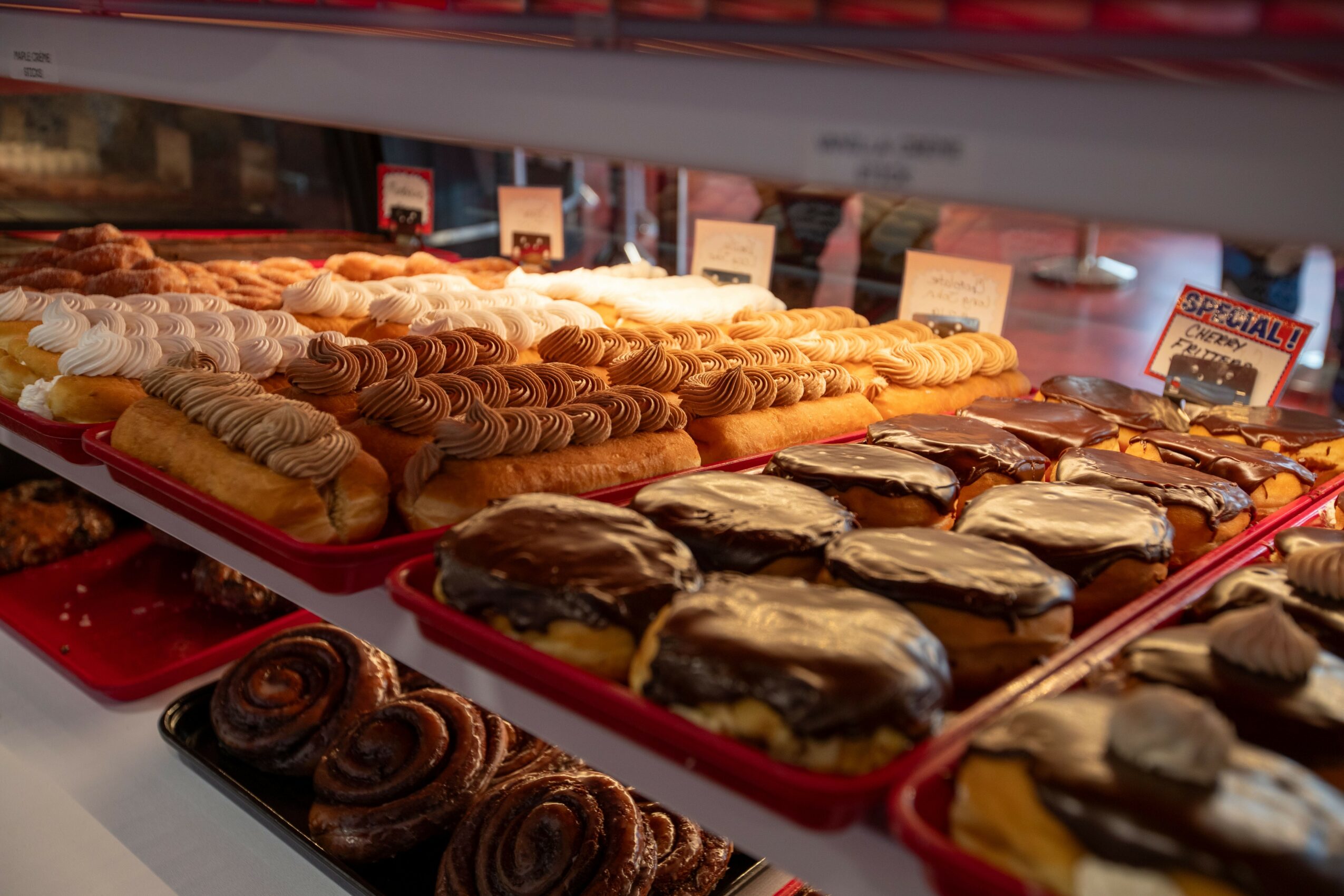 Display of assorted pastries including éclairs, cream puffs, and chocolate-covered treats on a bakery shelf.