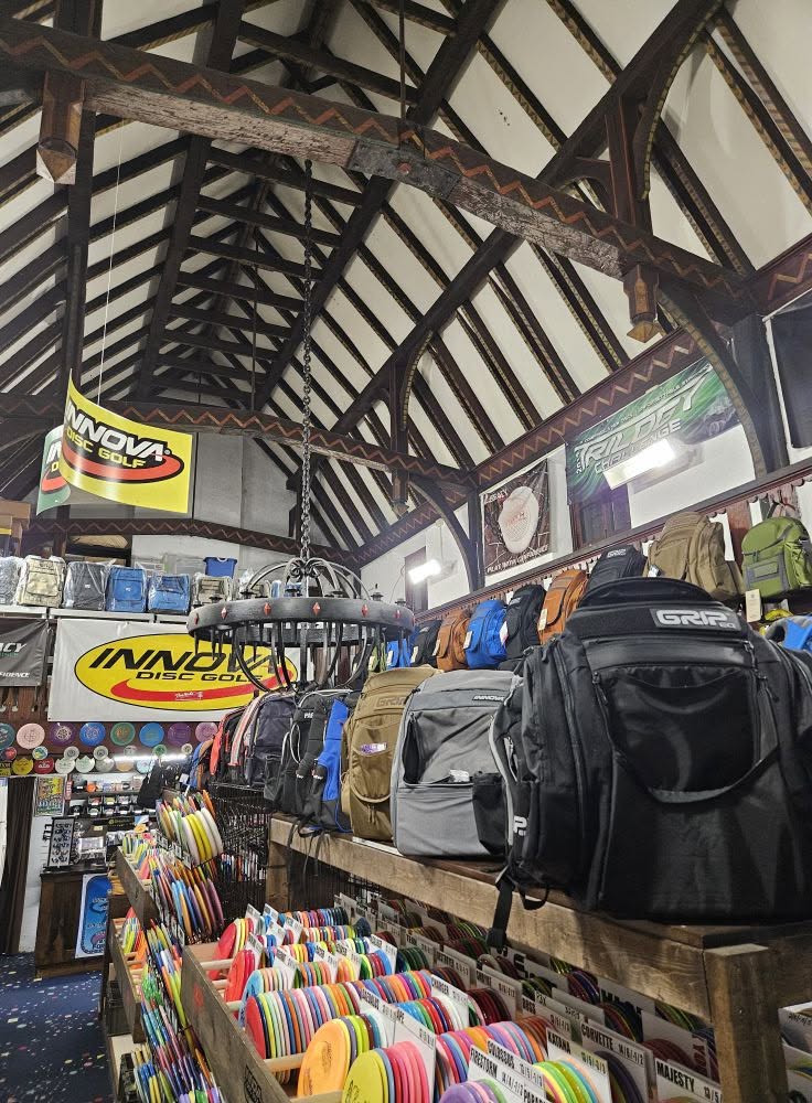 Indoor store with backpacks on shelves and colorful items in the foreground, wooden ceiling with beams, and banners hanging.