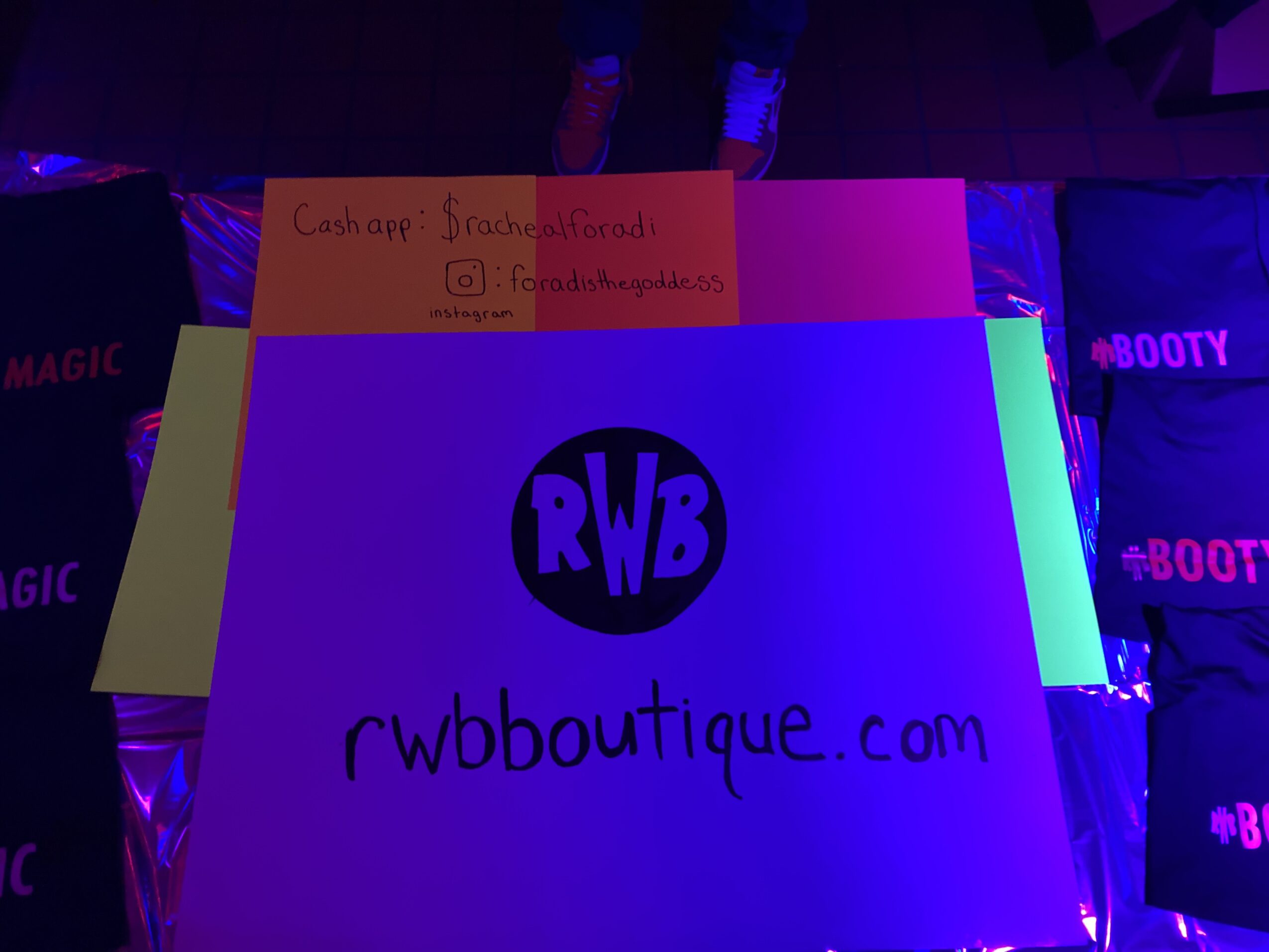 Sign with website and social media information, illuminated by colorful lights, with a logo reading 'RWB'.