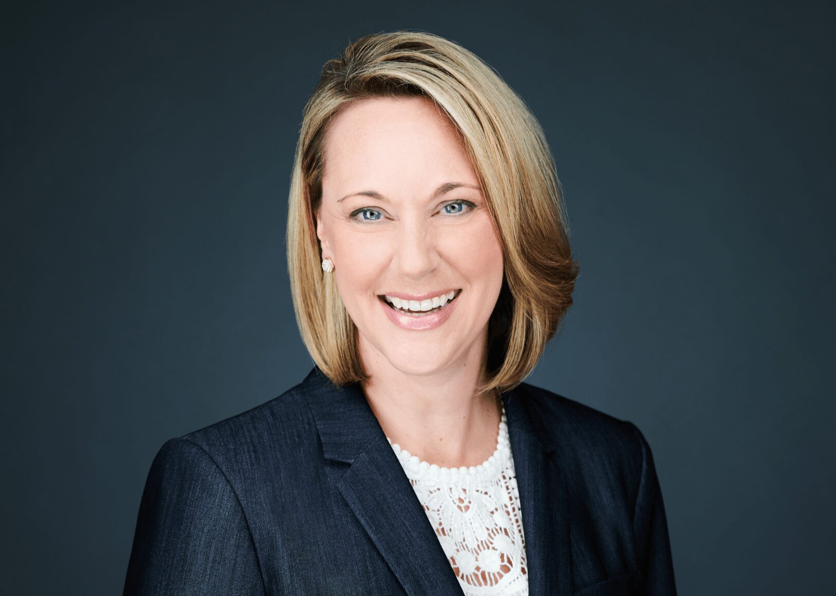 Portrait of a smiling woman with shoulder-length blonde hair wearing a dark blazer and white top.