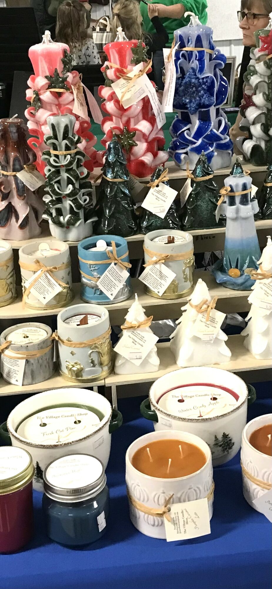 Display of decorative candles and gift boxes with ribbons, arranged on shelves, in various colors and designs.