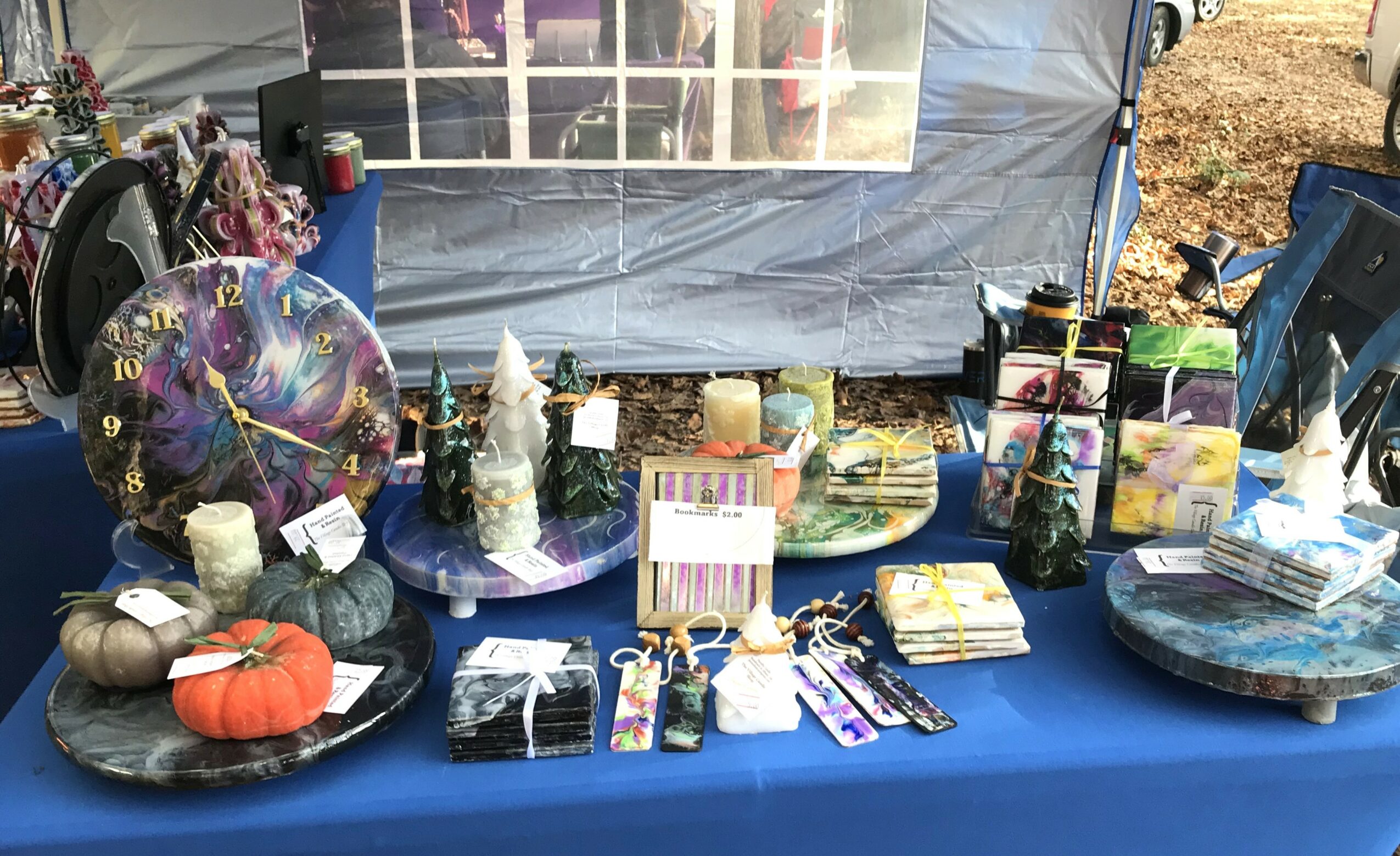 Table with various items including a pumpkin, candles, and decorative objects, set outdoors under a tent with a blue tablecloth.