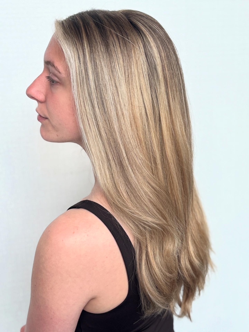Side view of a woman with long, straight blonde hair wearing a black top, against a light background.