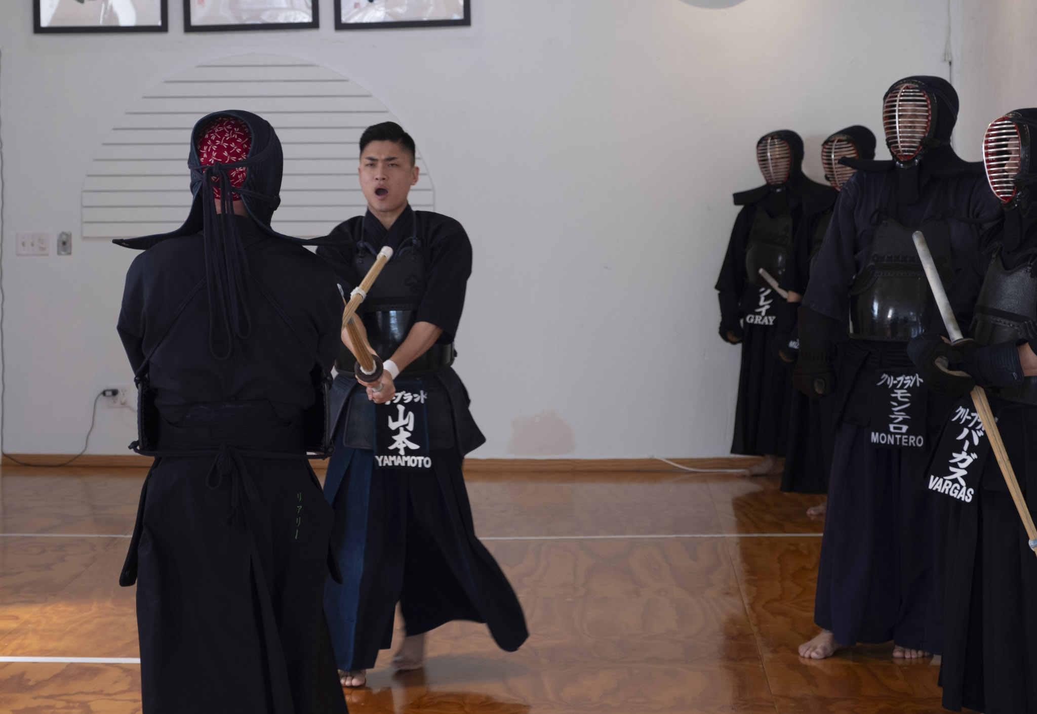People practicing martial arts with wooden swords in a dojo, some wearing masks and traditional clothing.