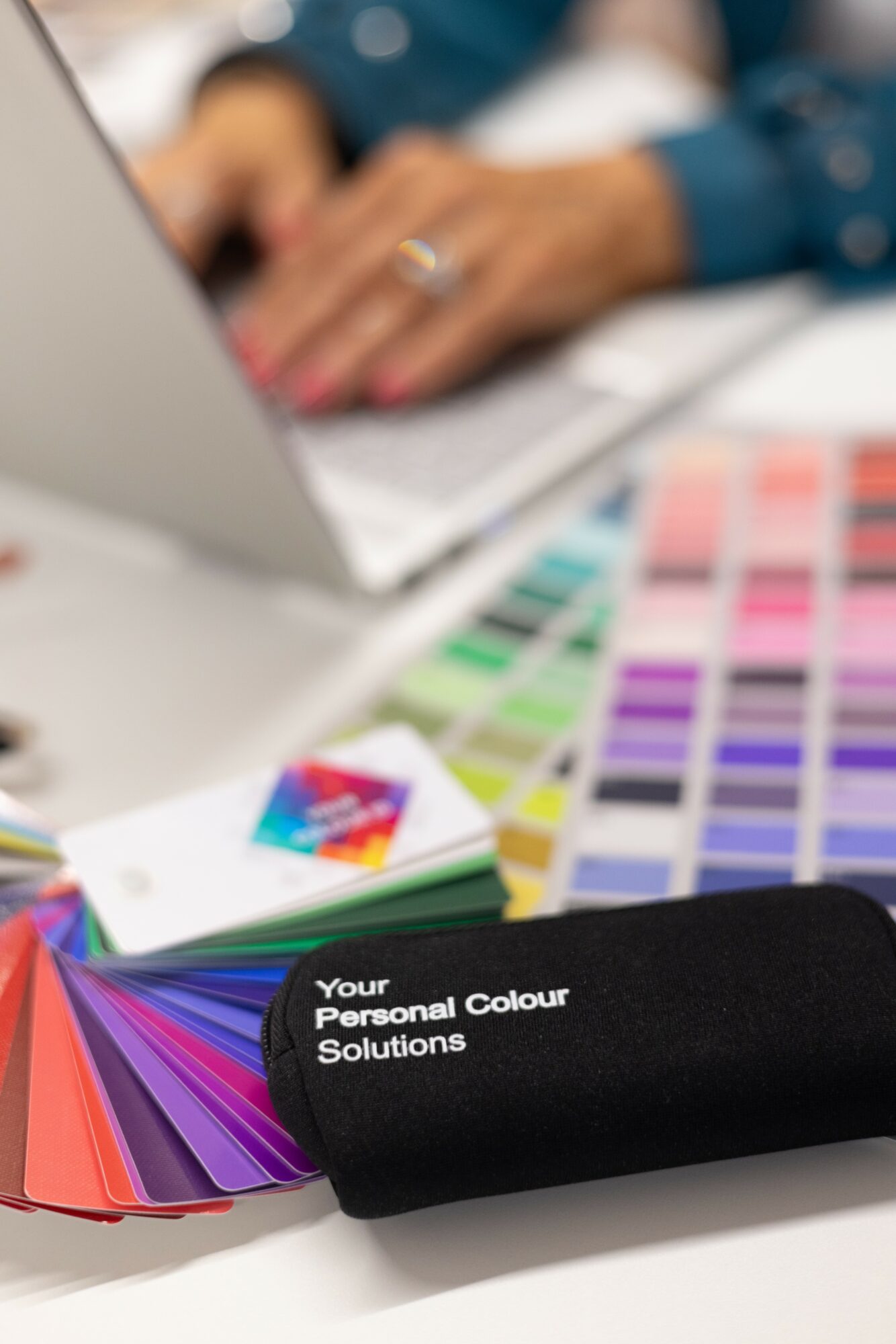 Color swatches and a fabric sample case on a table with a person working on a laptop in the background.