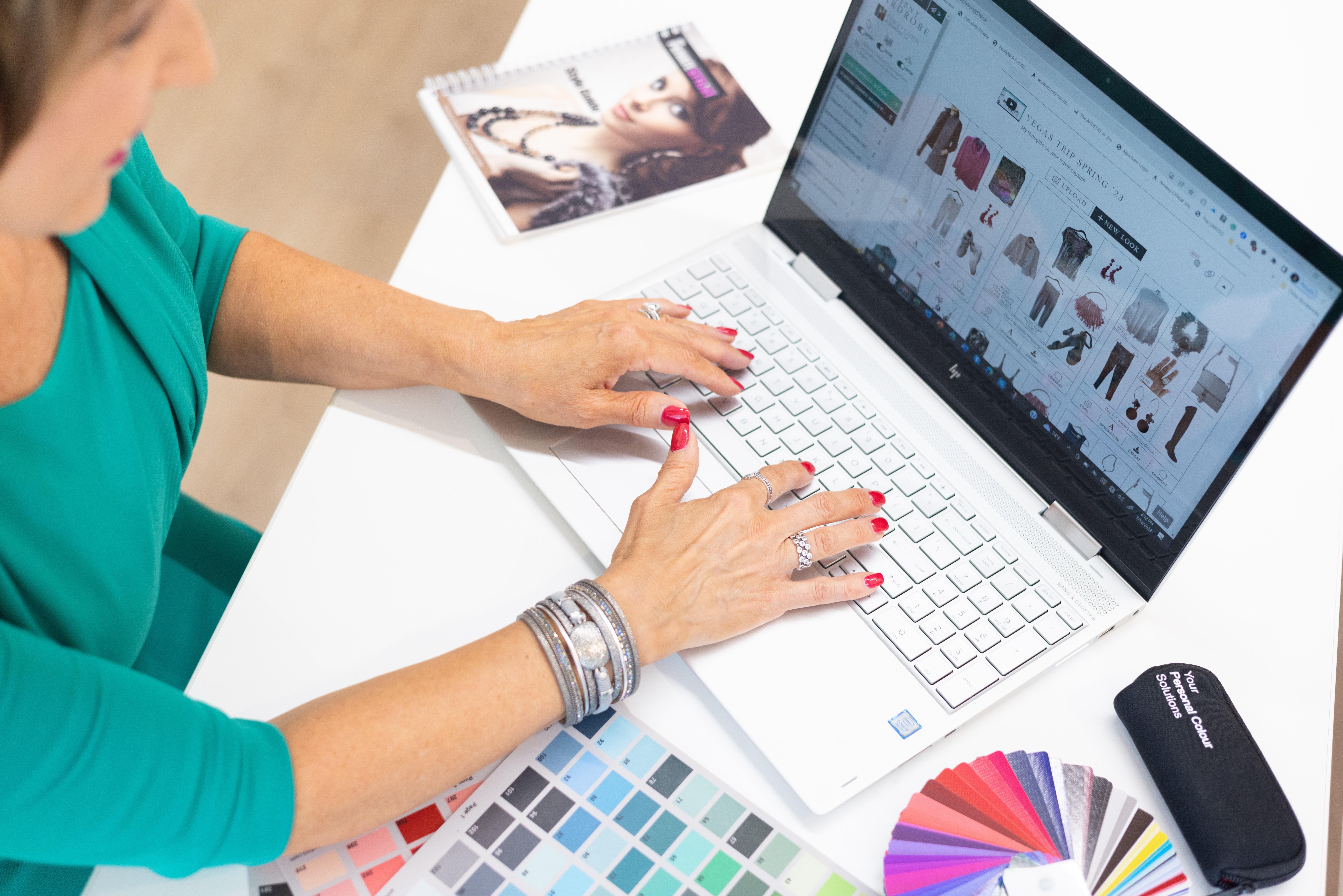 Person using a laptop with online shopping website open, shopping for clothes, with color swatches and a magazine nearby.