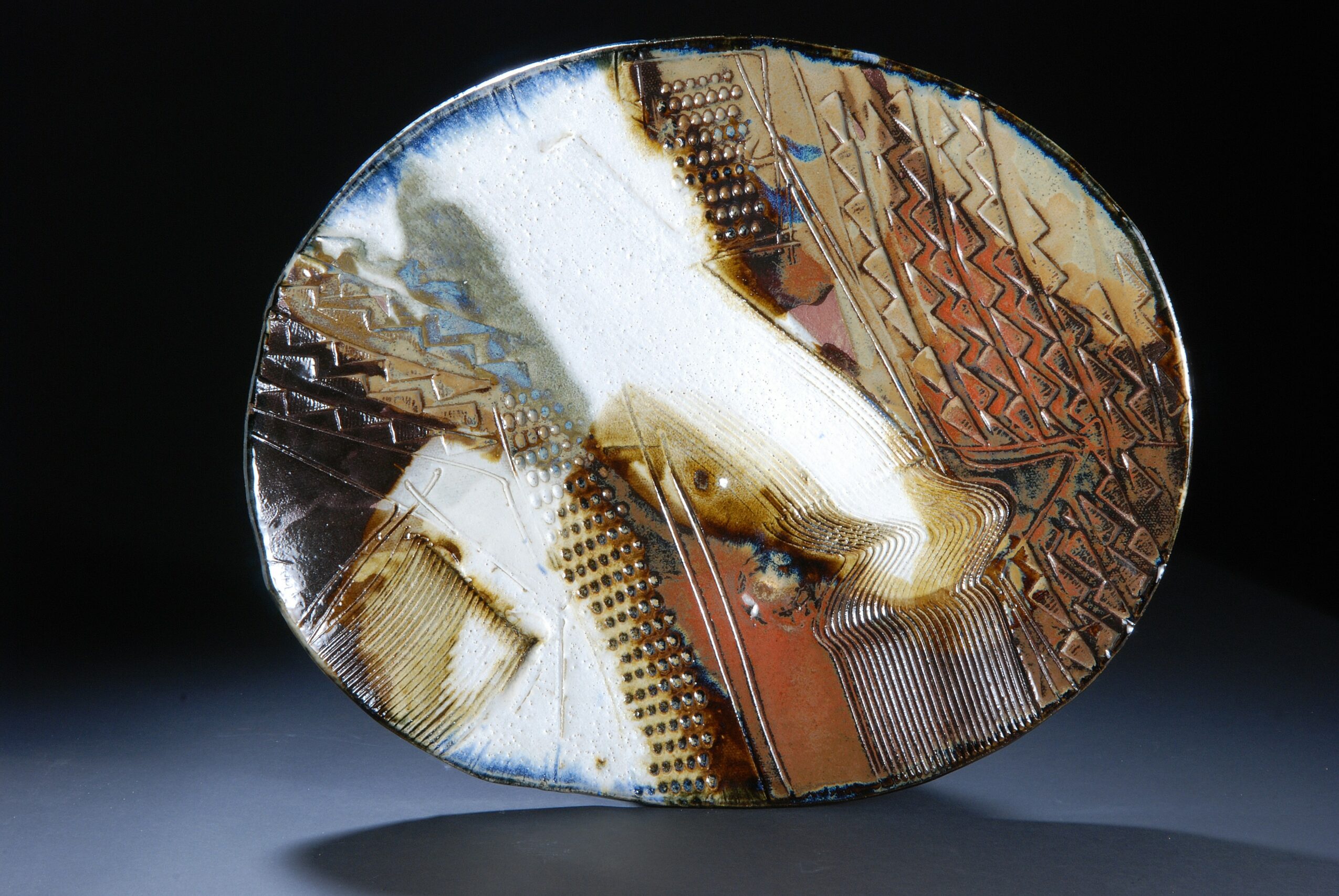 Decorative ceramic plate with abstract patterns and colors, placed on a surface against a dark background.