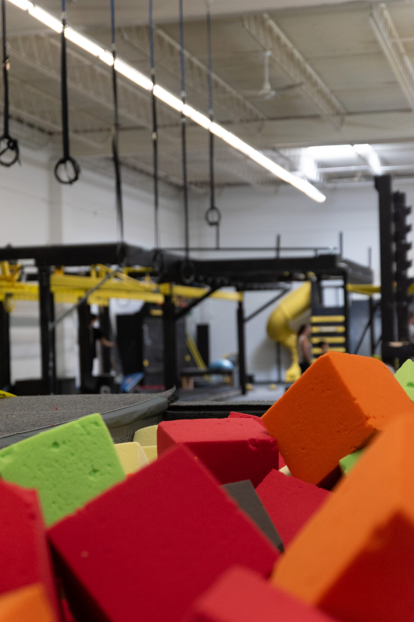 Colorful foam blocks in foreground with gym equipment and rings hanging from ceiling in background.
