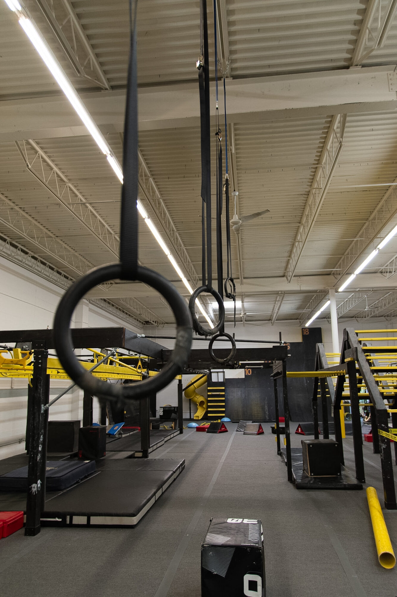 Indoor gym with hanging rings, workout equipment, and a high ceiling with lights.