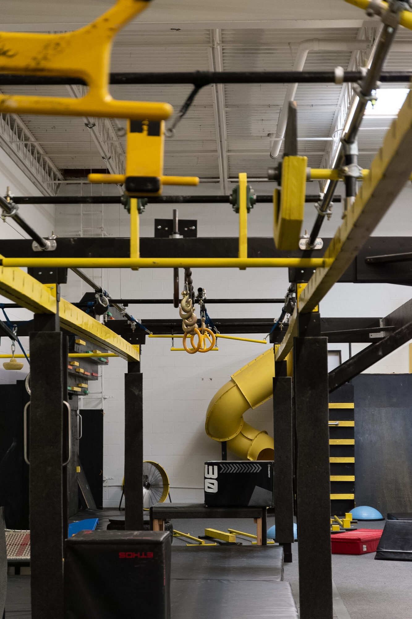 Indoor gym with yellow and black equipment, including a slide and hanging rings, in a spacious area.