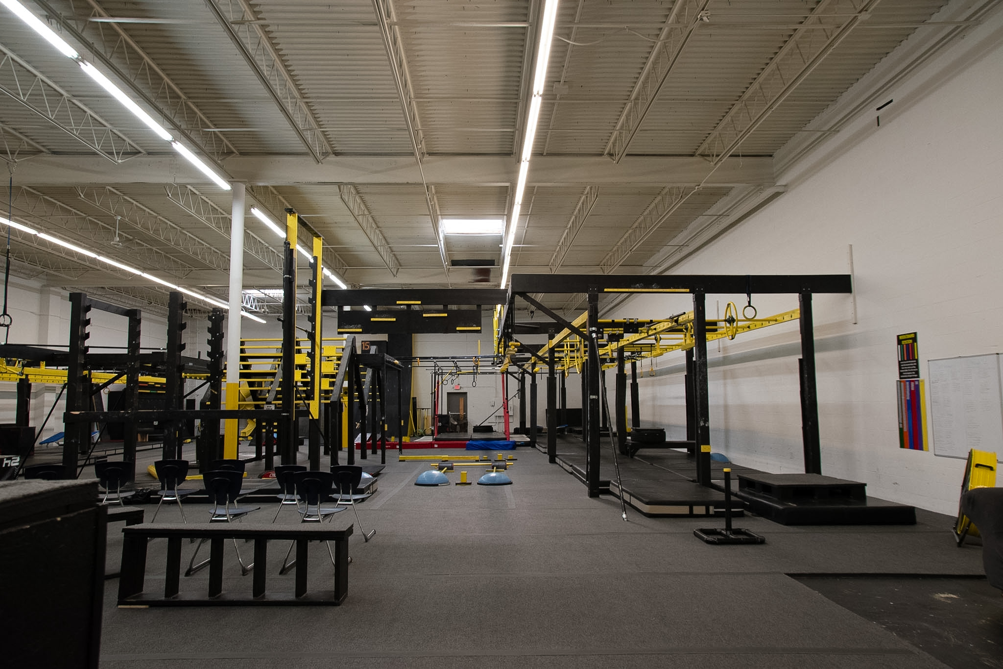 Empty gym with workout equipment, benches, and yellow and black structures in a spacious room.