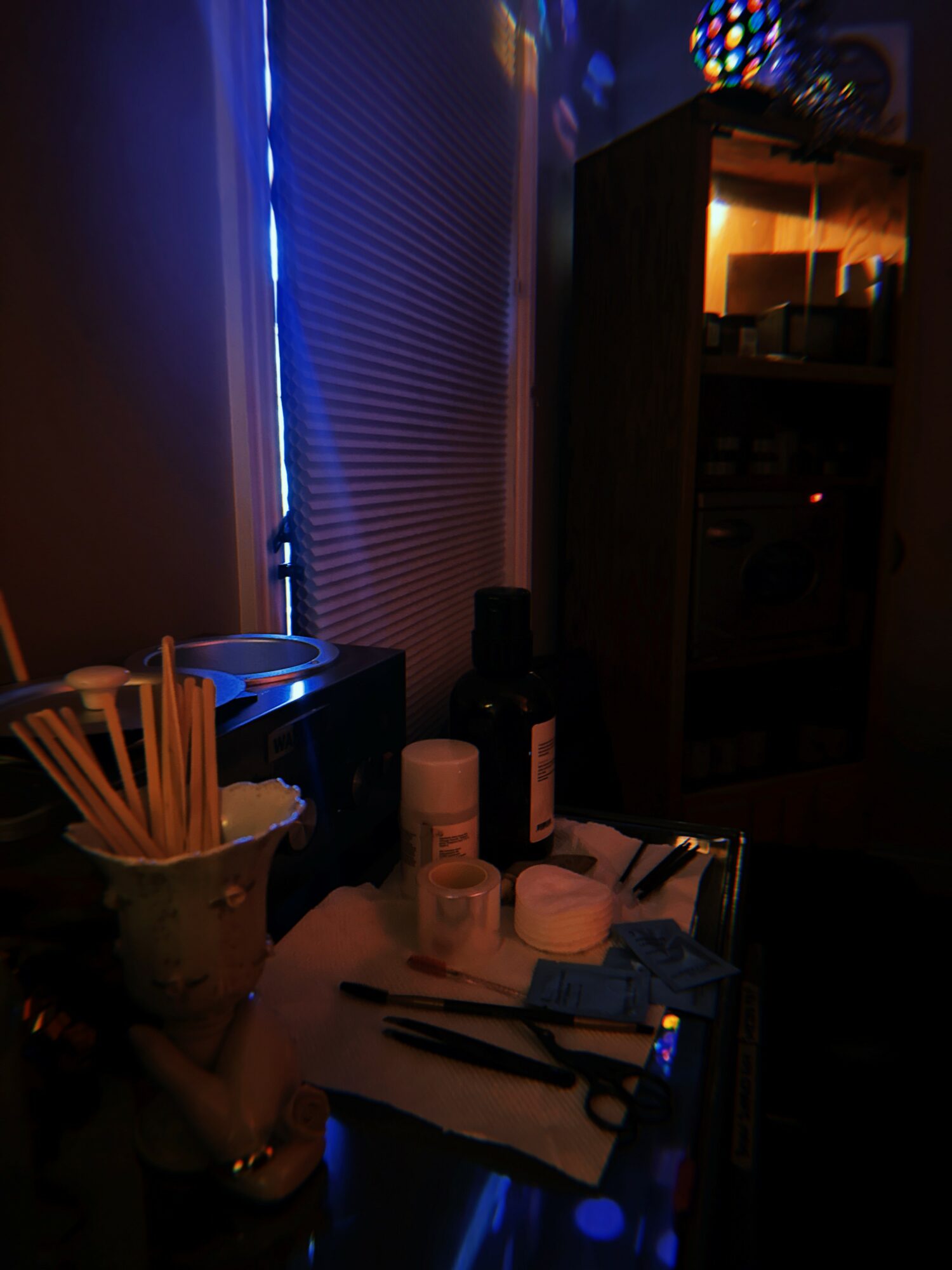 A cluttered table with bottles, utensils, and papers in a dimly lit room with blue and orange lighting.