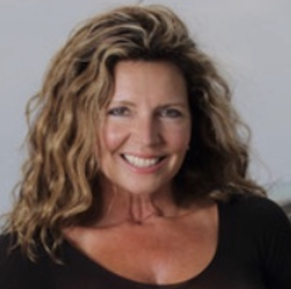 Woman with curly hair smiling, wearing a black top, against a light background.
