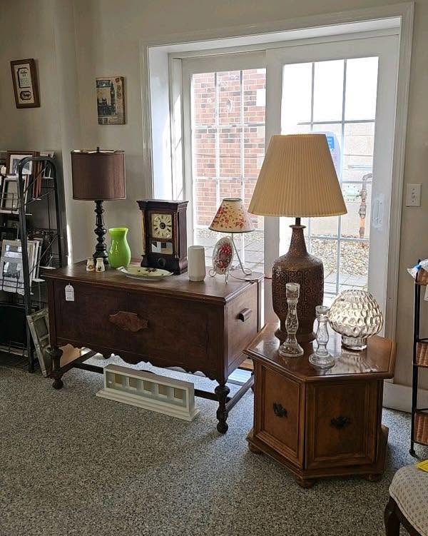 Living room corner with wooden furniture, lamps, and decorative items near a glass door, with a brick wall outside.