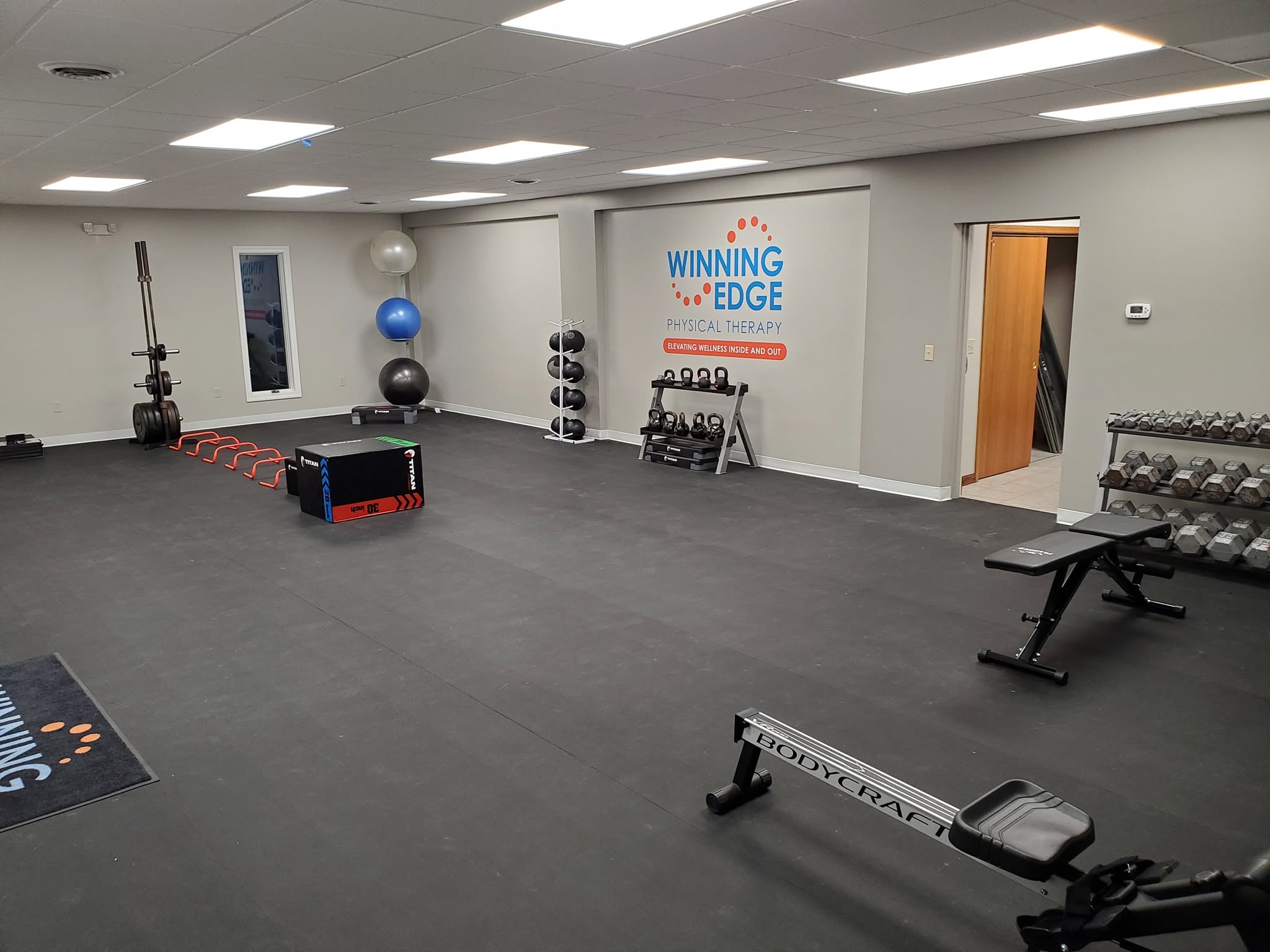 Gym room with exercise equipment, weights, and a motivational poster on the wall, well-lit with ceiling lights.