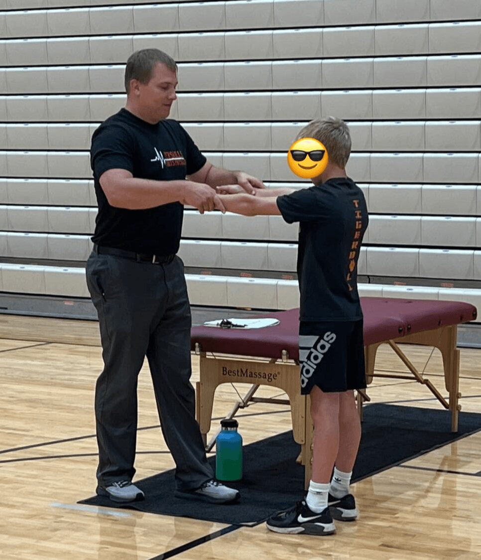 Adult and child holding hands in a gymnasium, with a massage table and water bottle nearby.