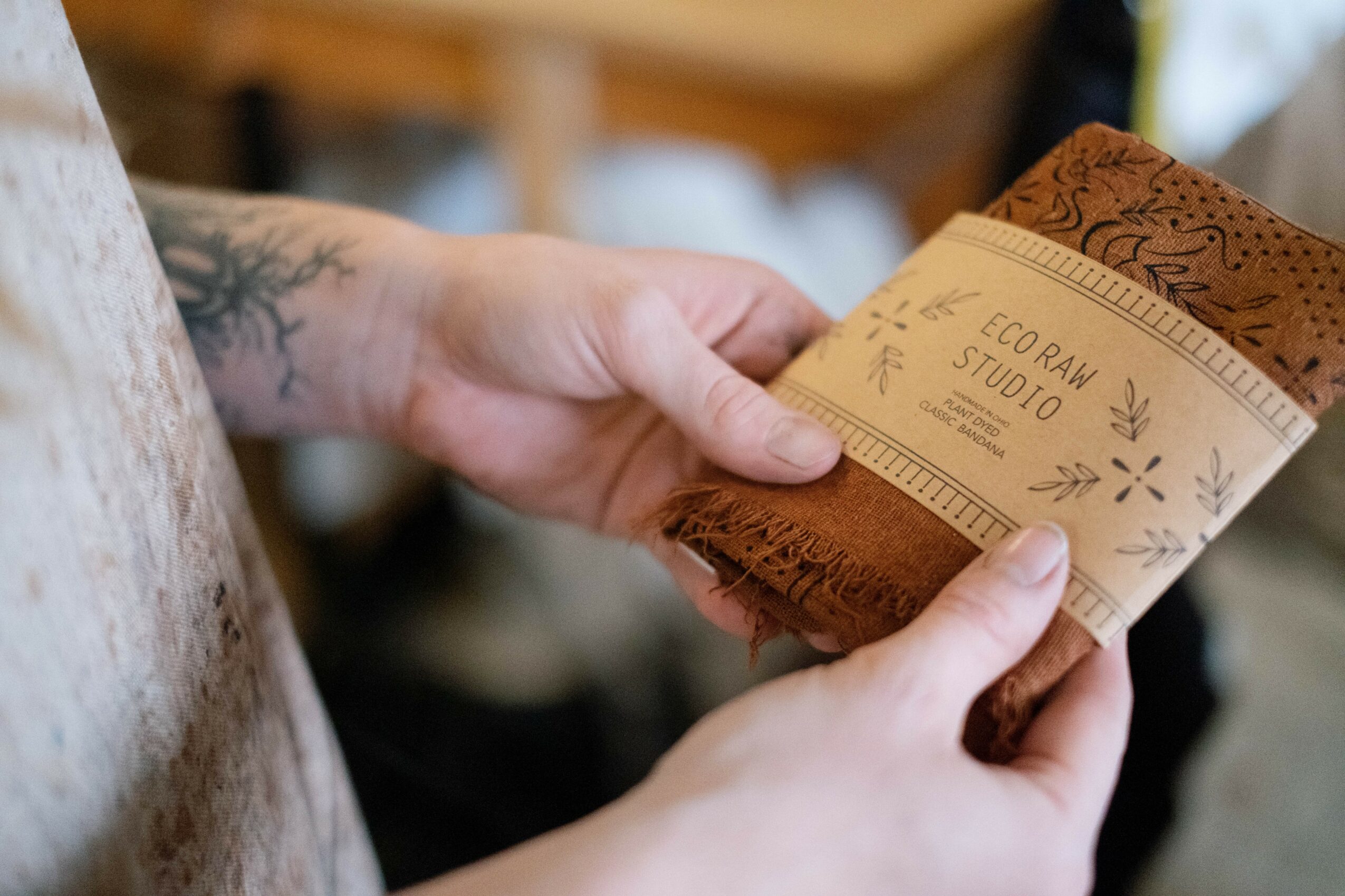 Person holding a brown leather wallet with a paper band reading 'CORN STUDIO' around it, tattoo visible on wrist.