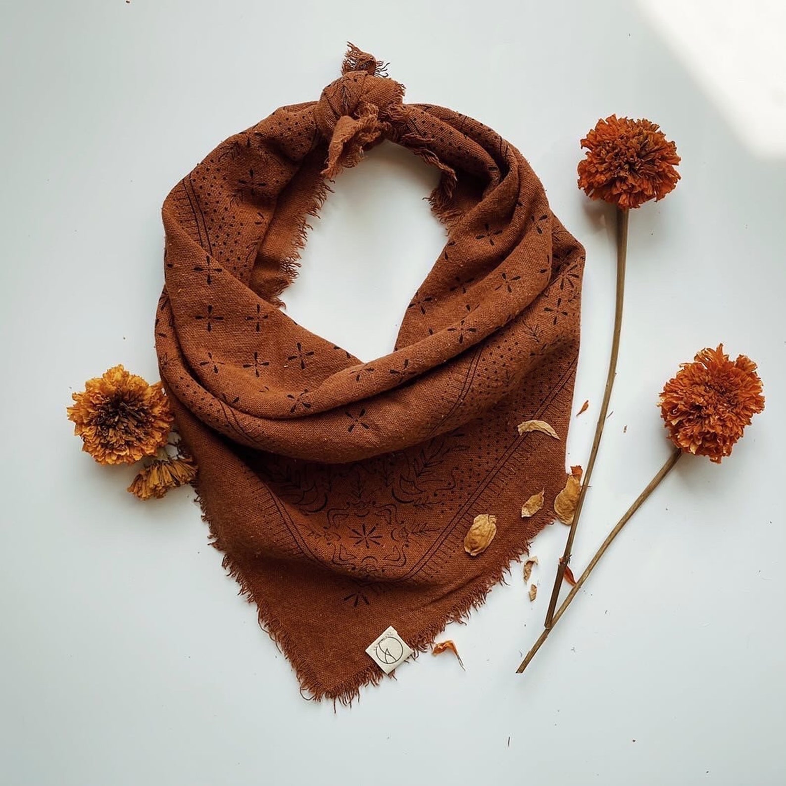 Brown scarf with floral pattern, three orange flowers, and a white background.