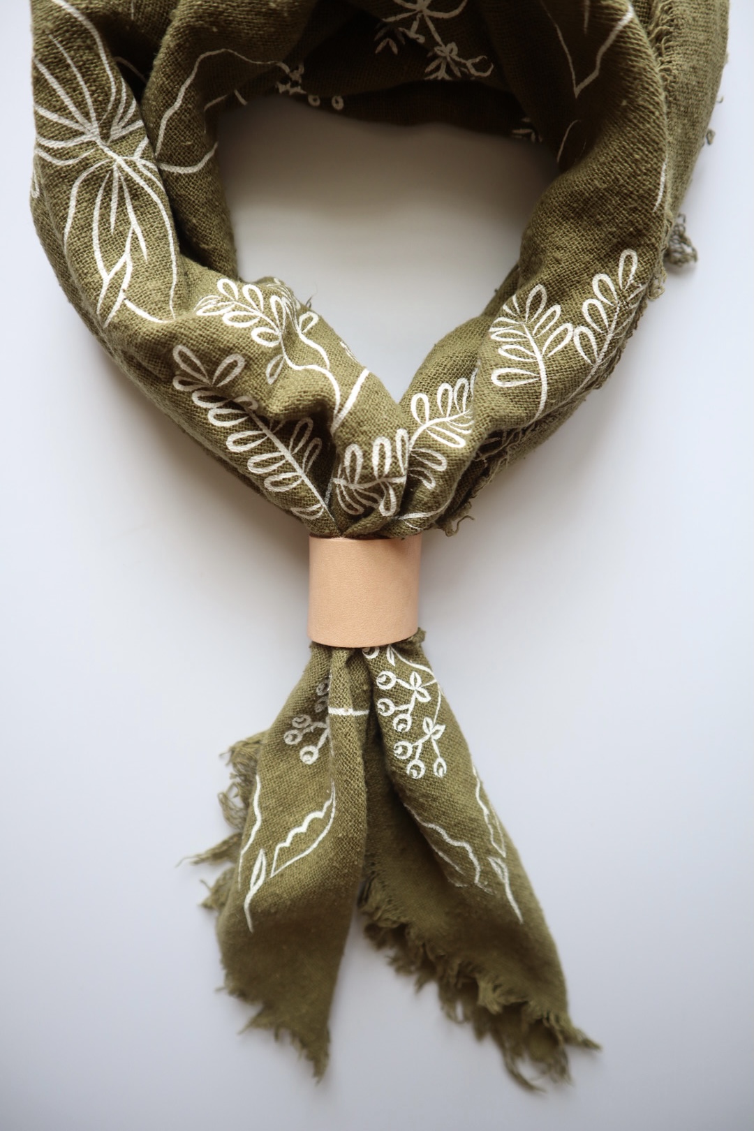 Olive green scarf with white embroidered floral patterns, tied with a pink band, displayed against a white background.