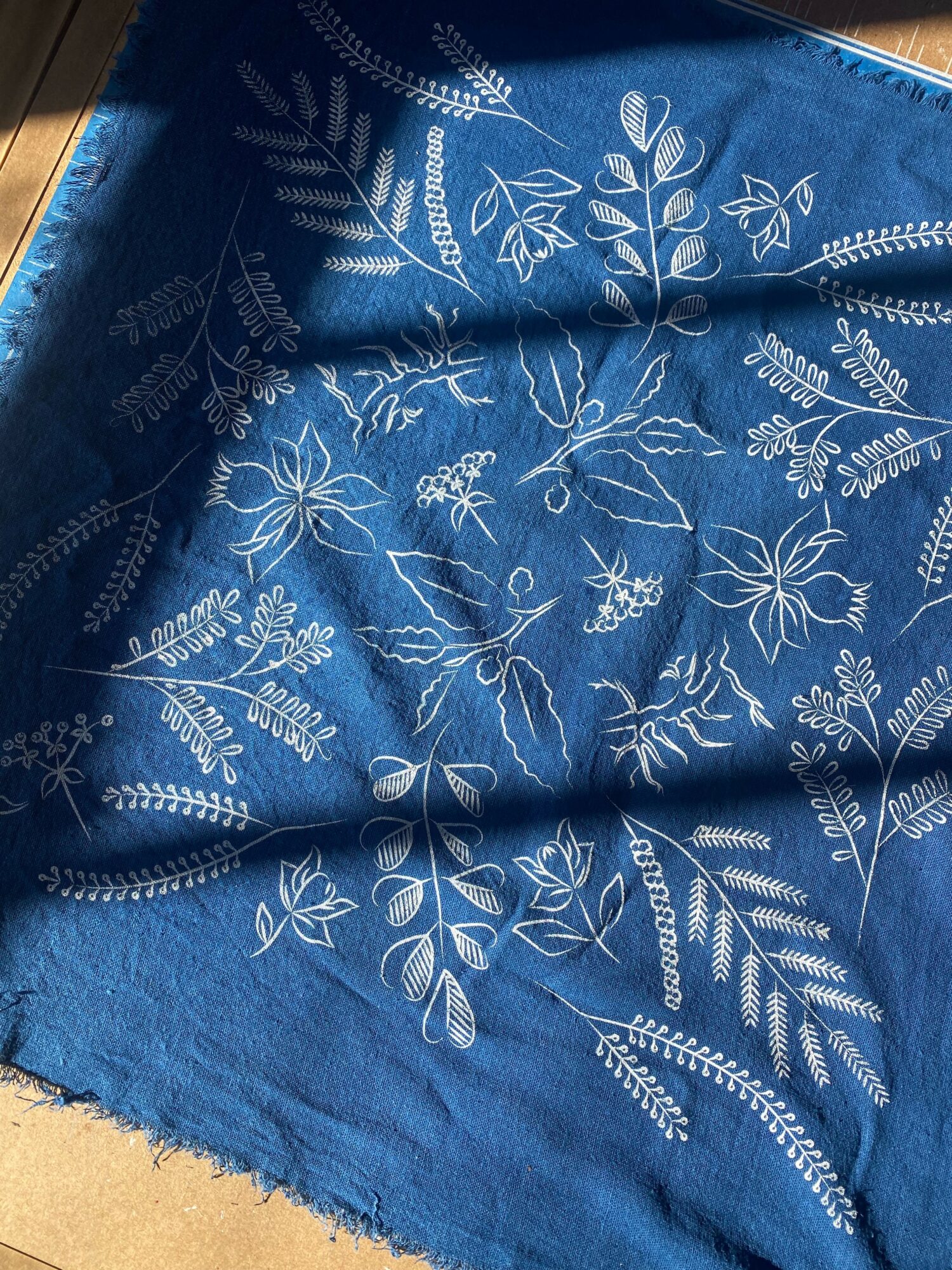Blue fabric with white floral and leaf patterns, slightly wrinkled, with a wooden surface visible at the top left corner.