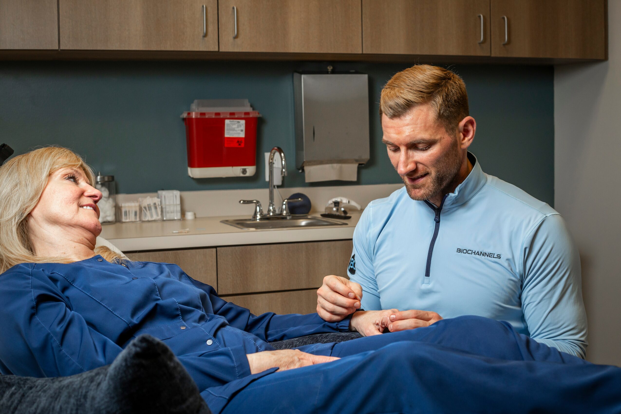 A woman lying in a hospital bed smiling at a man standing beside her, holding her hand, in a hospital room.