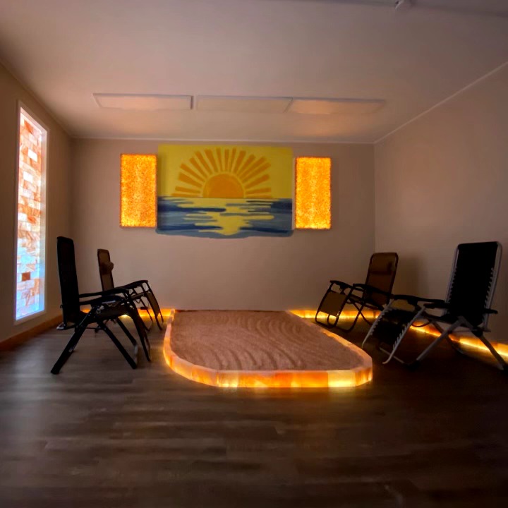 Room with a stage, chairs, and a sunset painting, illuminated by warm lighting, with a wooden floor and plain walls.