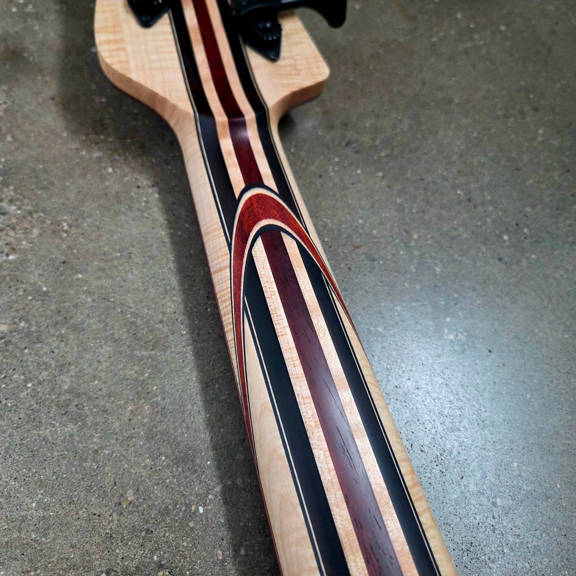 Close-up of a wooden guitar neck with colorful inlay design, lying on a gray surface.