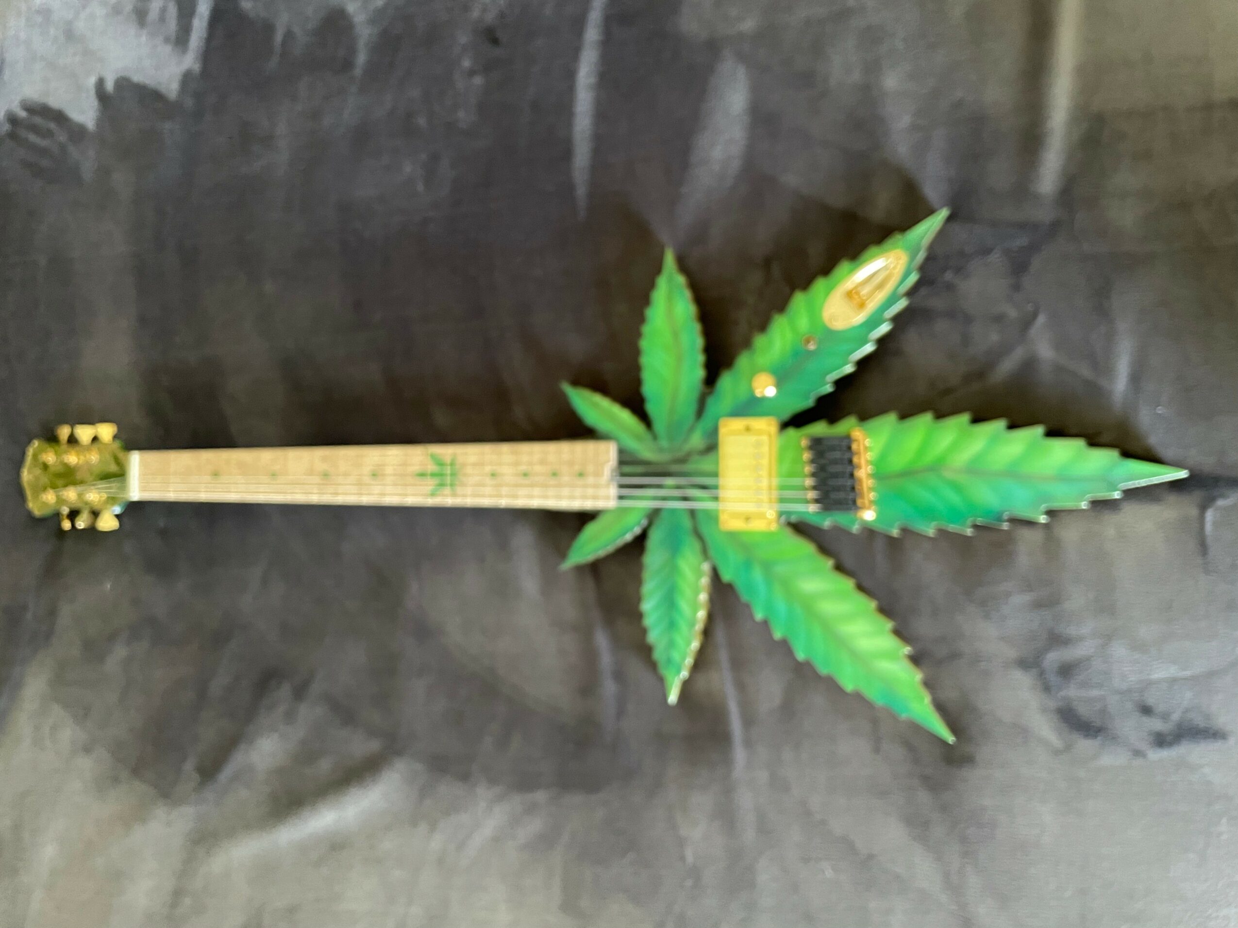 A novelty guitar with a body shaped like a cannabis leaf, lying on a dark surface.